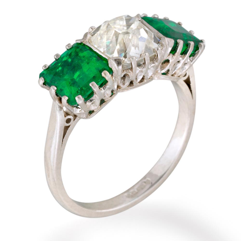 A diamond and emerald ring three stone ring, the central cushion shaped old cut diamond weighing 2.04cts, flanked by two rectangular mixed cut emeralds, total weight 2.4cts, all in a claw set mount, with cheniered shoulders on plain shank,