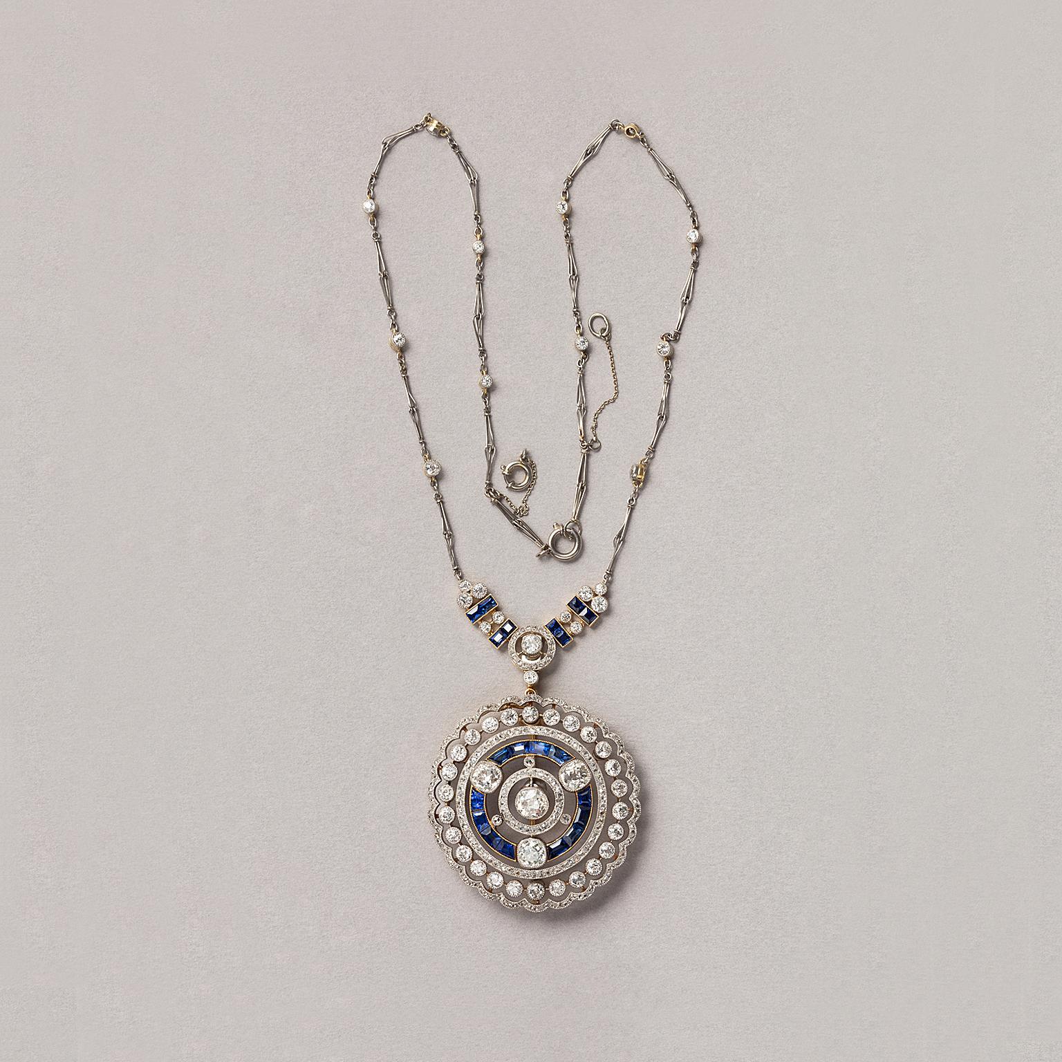 An 18 carat yellow gold and platinum Edwardian brooch or pendant and necklace, a round pendant with several circles mille griffe set with old and rose cut diamonds (app. 5.25 carat) and with tapered baguette cut sapphires. Around the center are