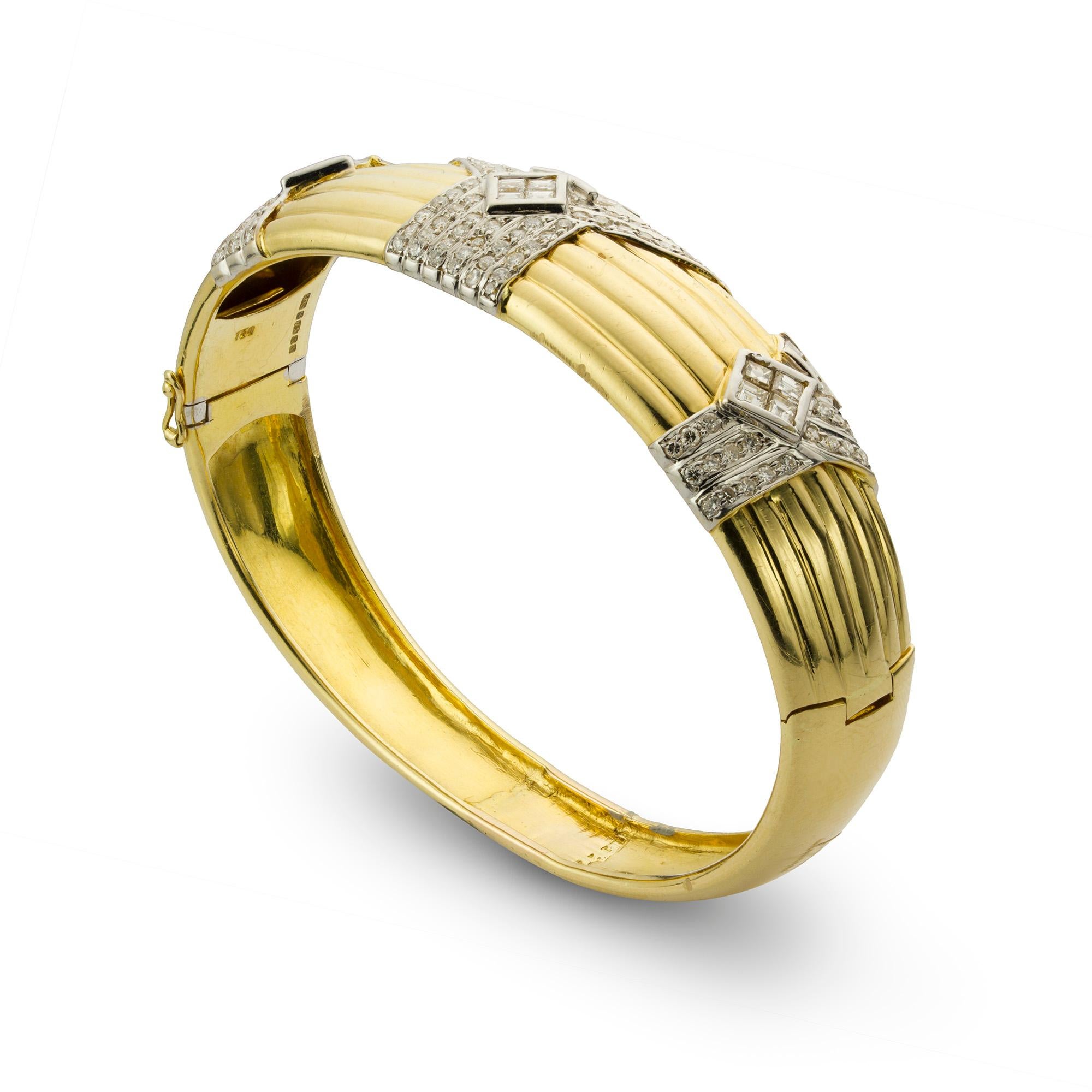 A diamond set 18ct yellow gold ribbed bangle, to the centre a diamond set spray detail with round brilliant-cut, square-cut and baguette-cut diamonds each set in 18ct white gold between two further diamond set sections leading to a plain yellow gold