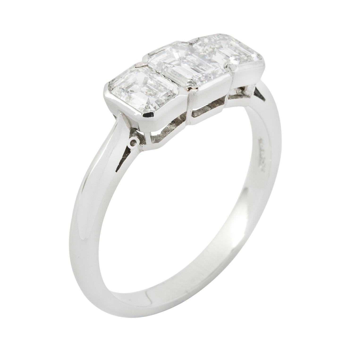A diamond three stone ring, the three graduating emerald-cut diamonds, weighing a total of 1.15 carats, rub over set to a platinum mount, with cheniere shoulders, hallmarked platinum London 2012, bearing the Bentley and Skinner sponsor mark, head