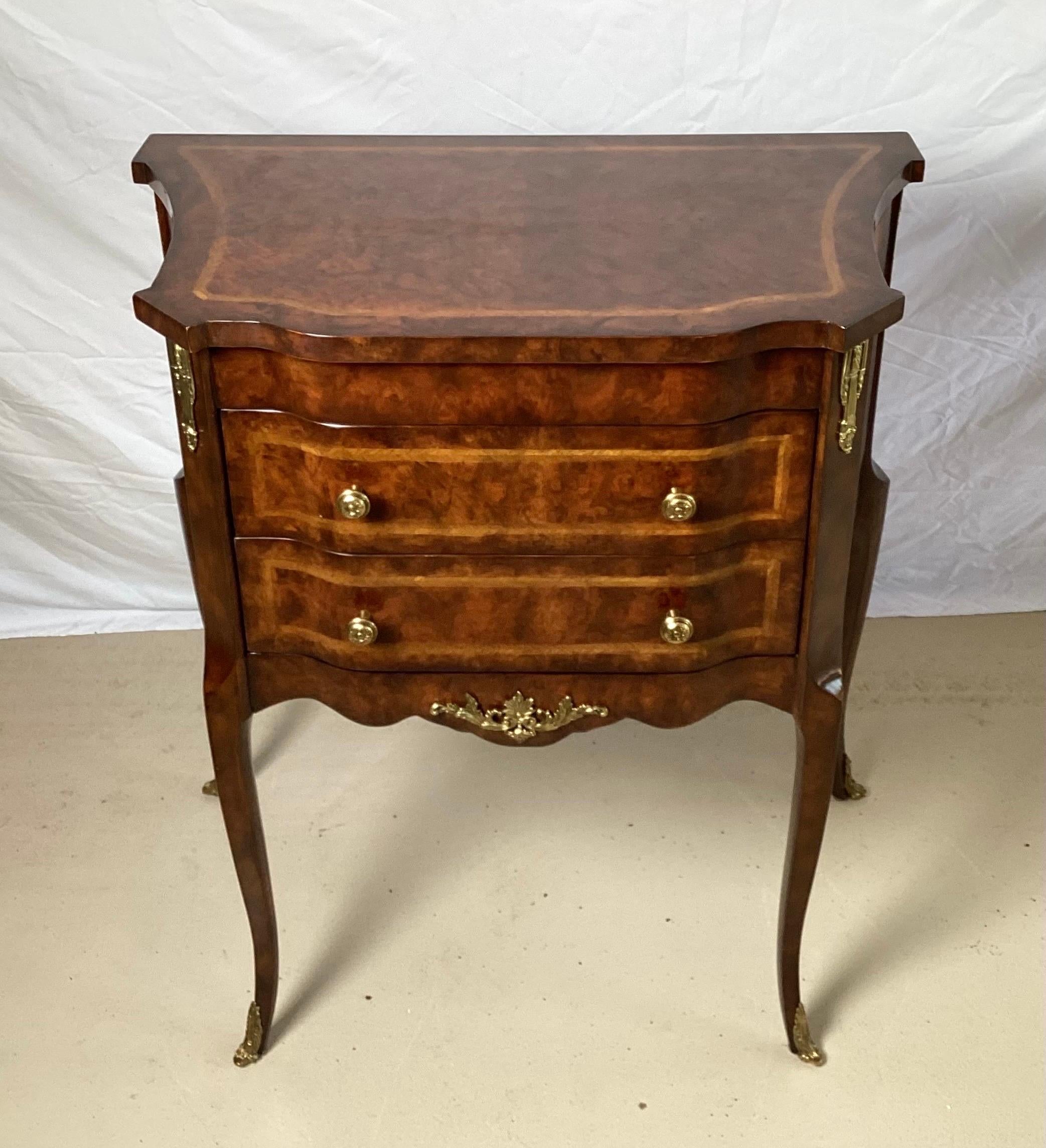 A diminutive two drawer Napoleon III style commode by Maitland Smith. The warm burl walnut with crass banded inlay with ormolu mounts. Shapely front with curved sides with gently curved and flared legs.