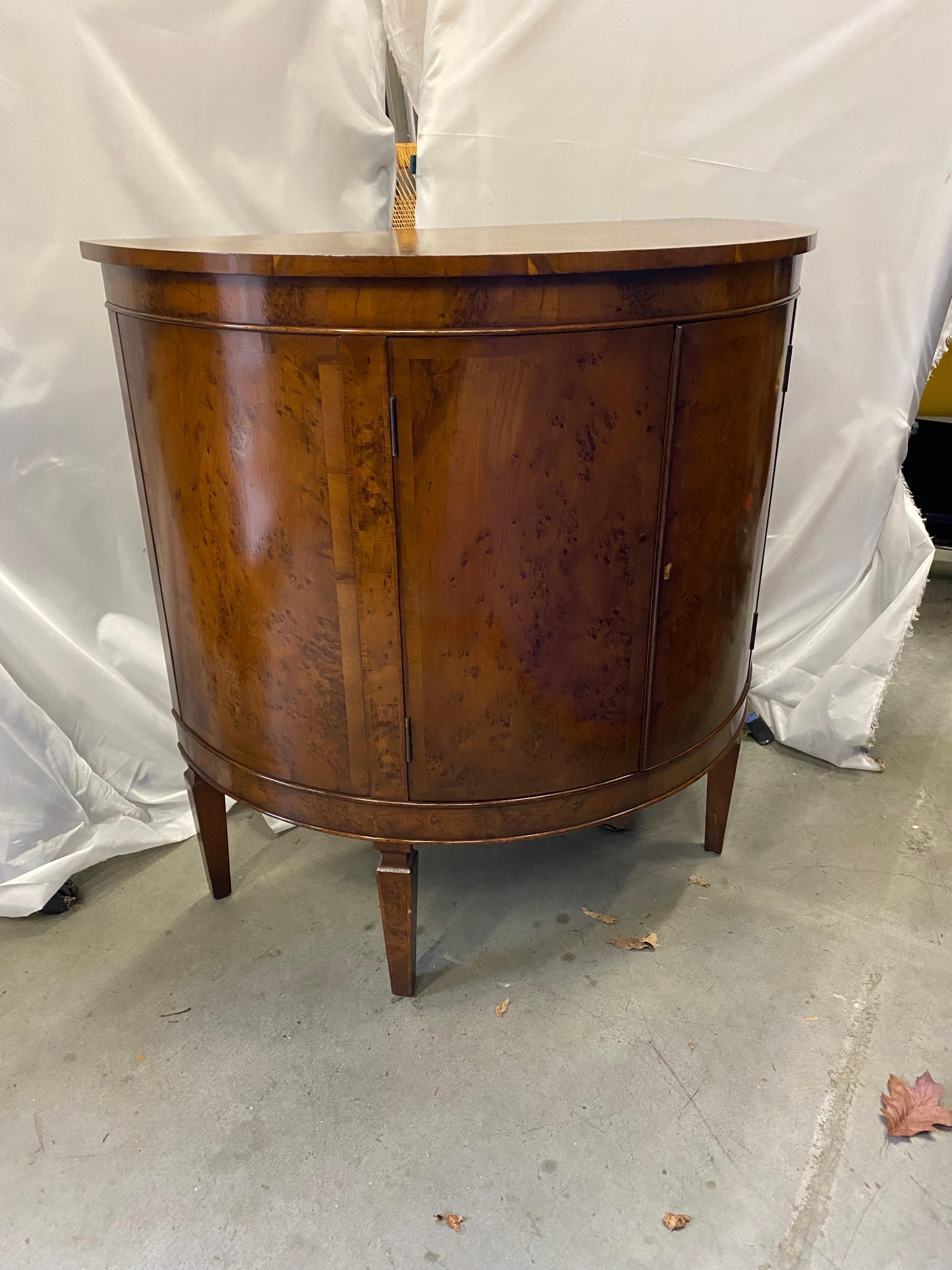 A handsome demilune commode with two doors and storage in a rich burl walnut.  The early 20th Century cabinet in a smaller size measuring 33 inches wide.  The highly figurative burl wood with cross banding inlay on the half circle top, with 2 doors