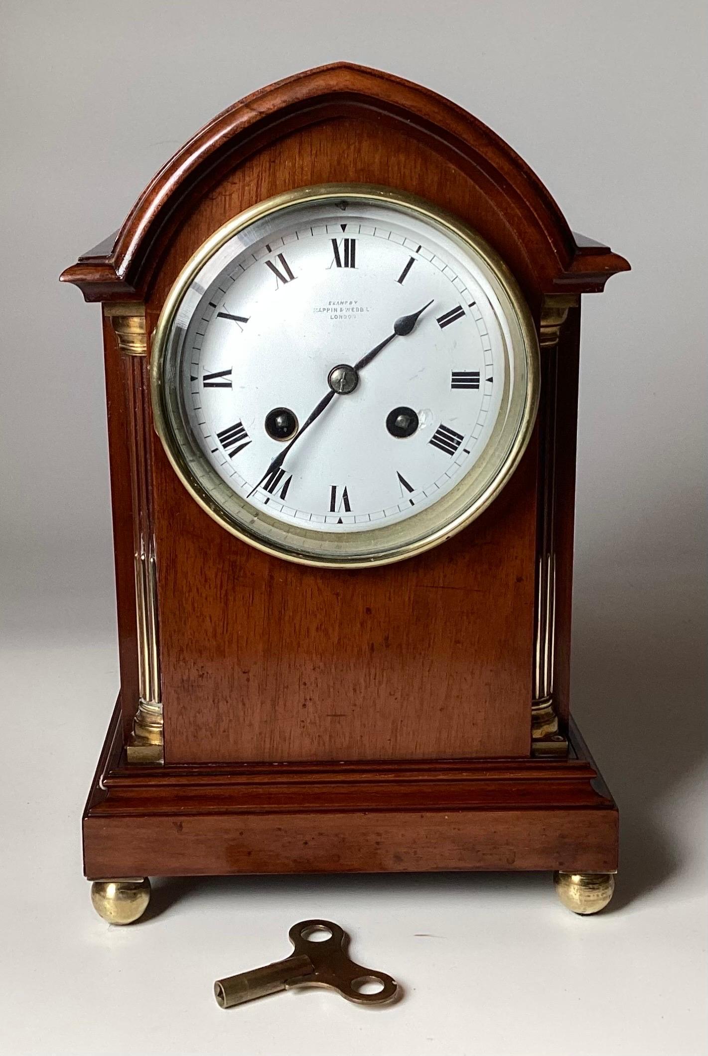 A Diminutive French Mahogany Mantel Clock, Retailed by Mappin & Webb, London, Late 19th Century. The George III style case in the Gothic taste with carved and brass stop-fluted quarter columns, raised on small brass ball feet. The The circular white