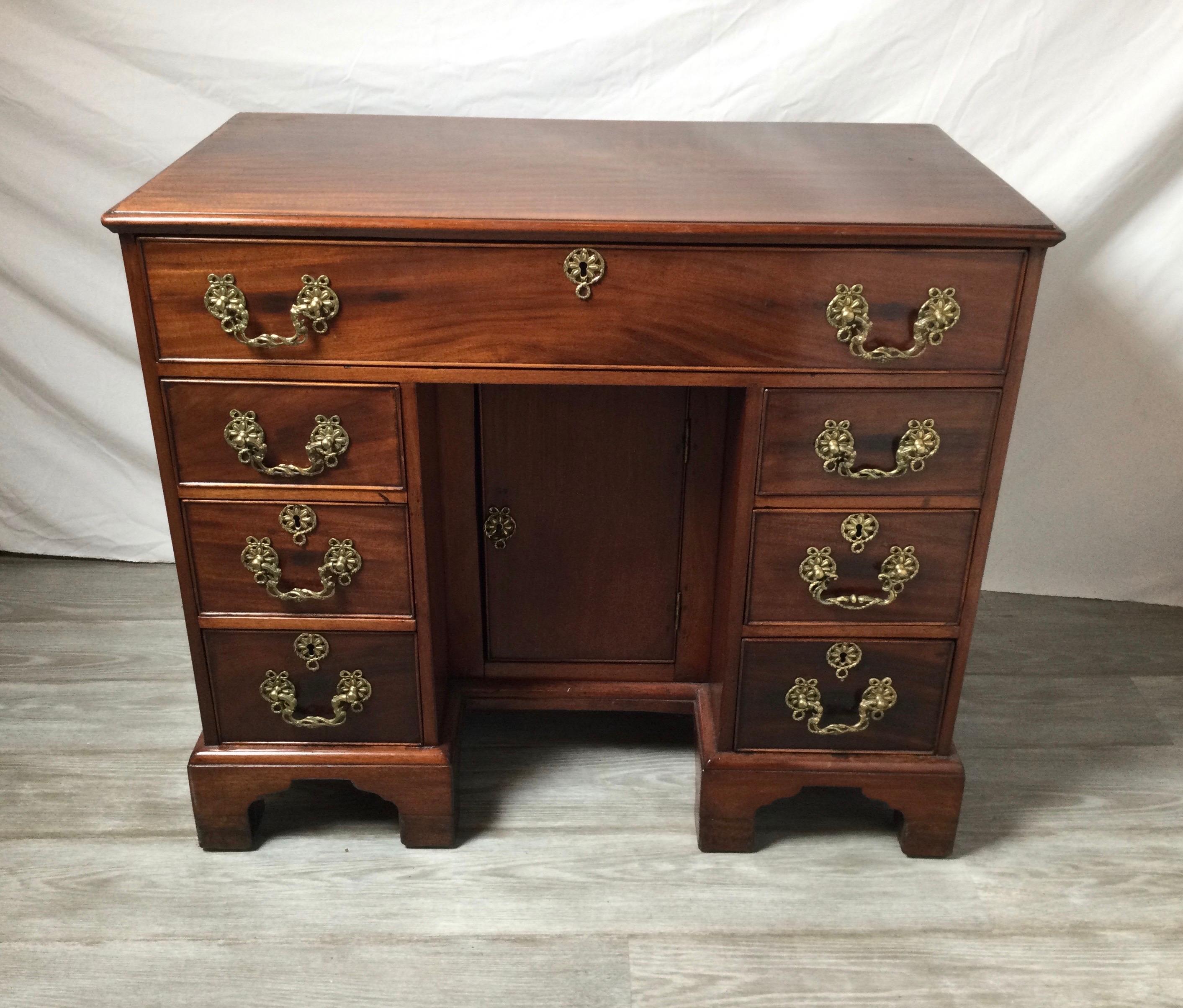 An English mahogany desk, circa 1780. A rectangular top with one long drawer with three smaller drawers on each side. There is a center door storage compartment in the cent. The desk with brass hardware and key, all resting on four bracket feet. An