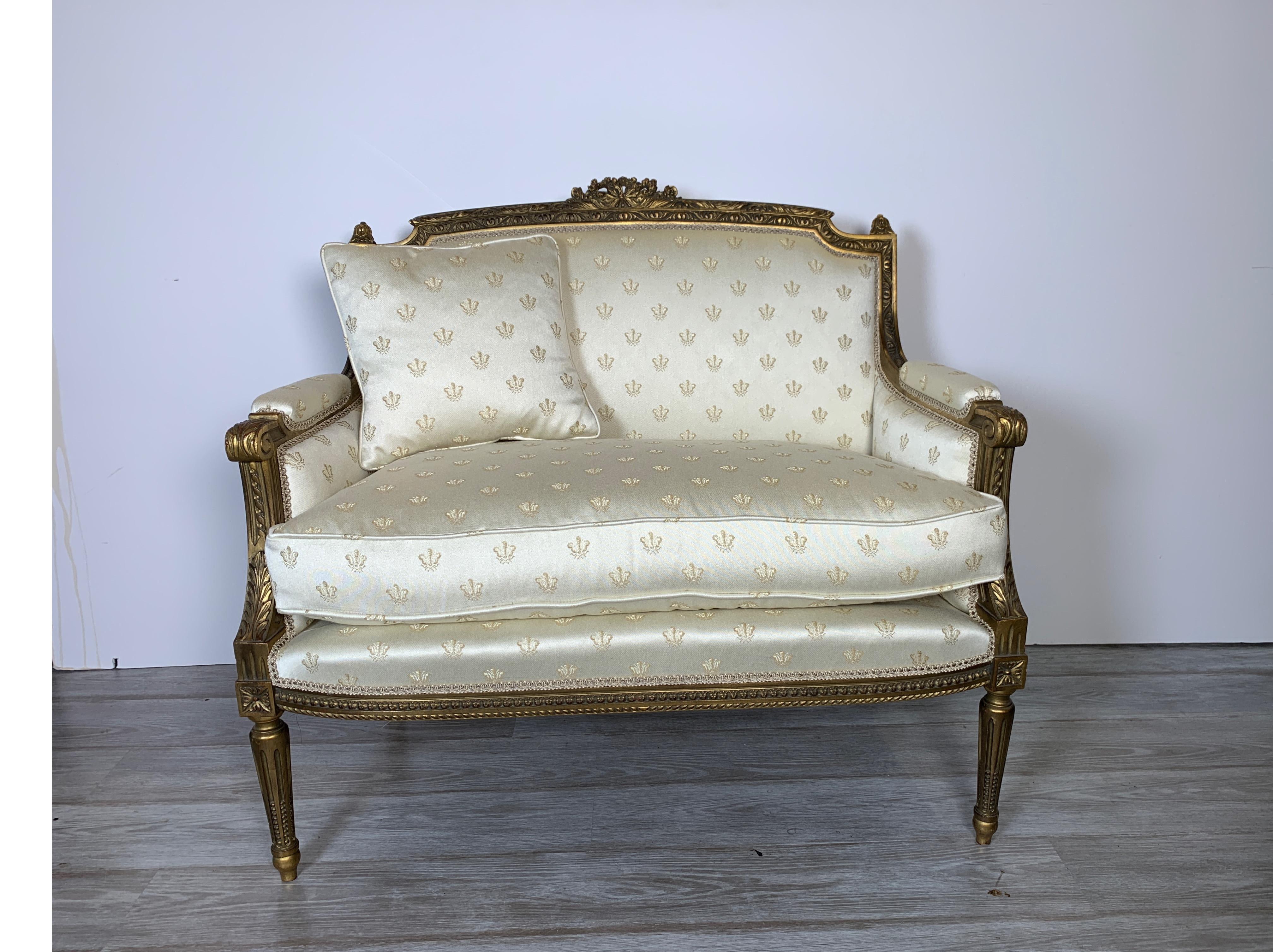 A diminutive giltwood settee in the Louis XVI style. The gold frame with carved detail all along the frame. The upholstery is newly covered with a napoleon bee damask in oyster white.