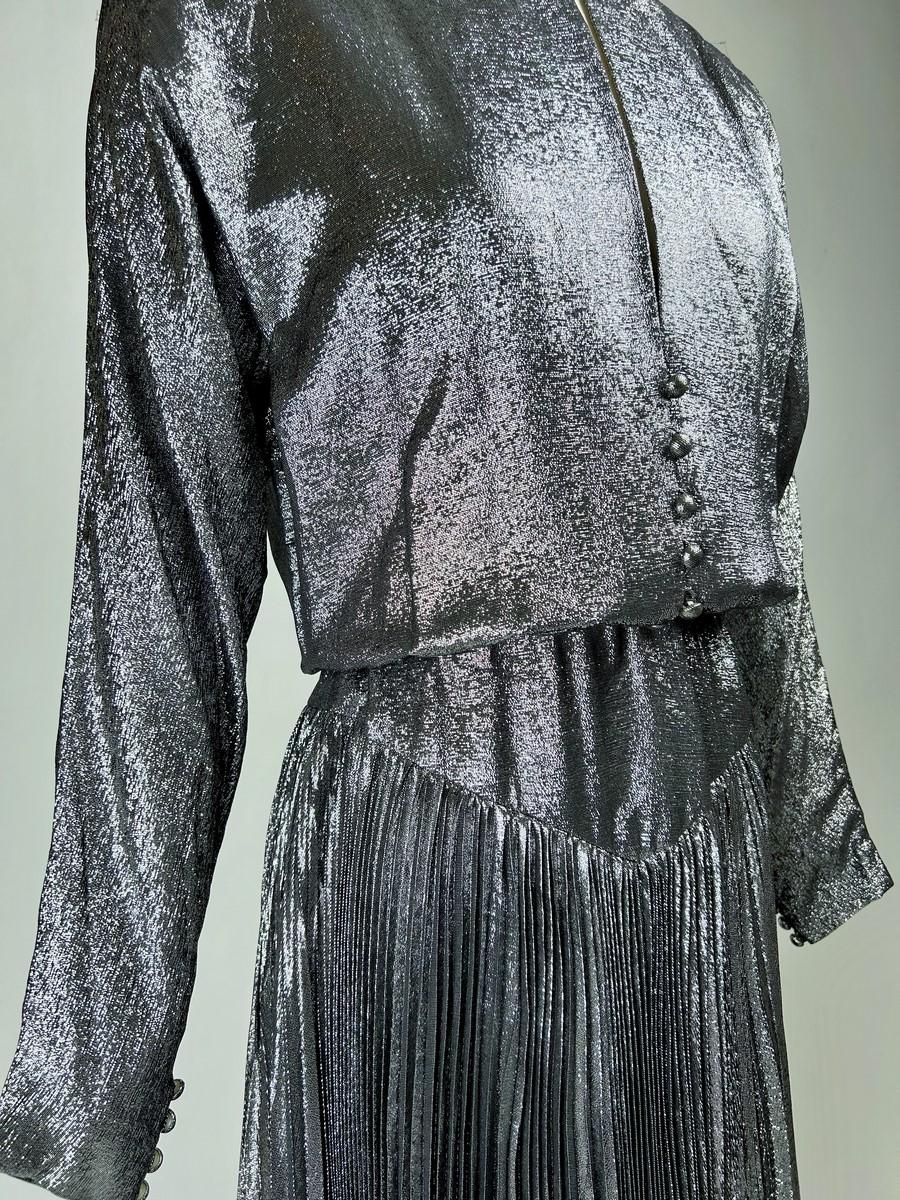 Circa 1985

France

Disco ball gown by Jean-Louis Scherrer Boutique numbered 302451 in silver silk and polyester lamé. Blousante dress with batwing sleeves and Mao collar with a plunging slit on the chest. On the hips, a V-shaped cut-out is held in