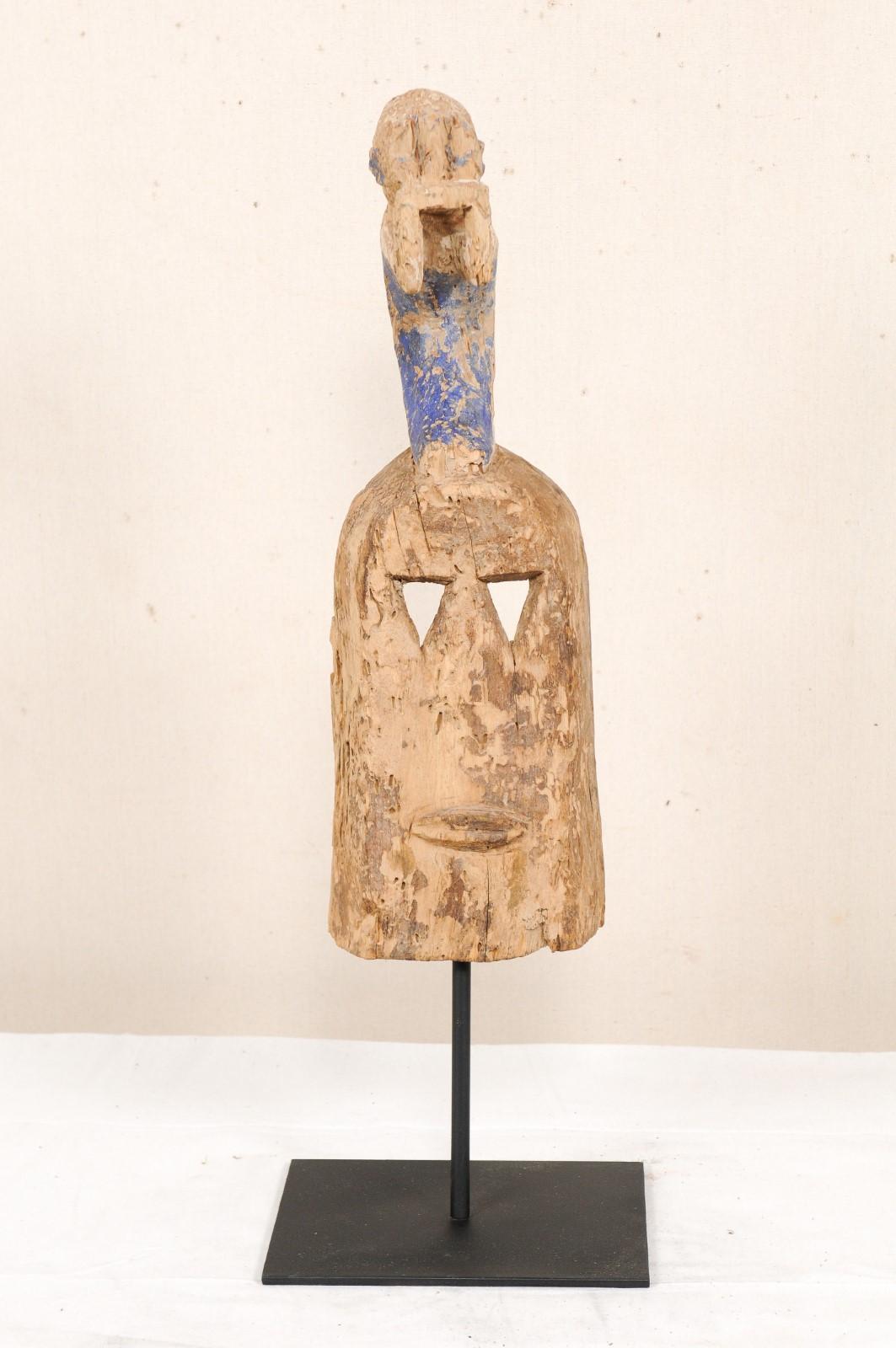 A Dogon Mali dance mask with carved figure from the early to mid 20th century. This Dogon tribal wooden ceremonial dance mask originates from Mali, West Africa. The mask is hand-carved and features a face with triangular eye holes, which is topped