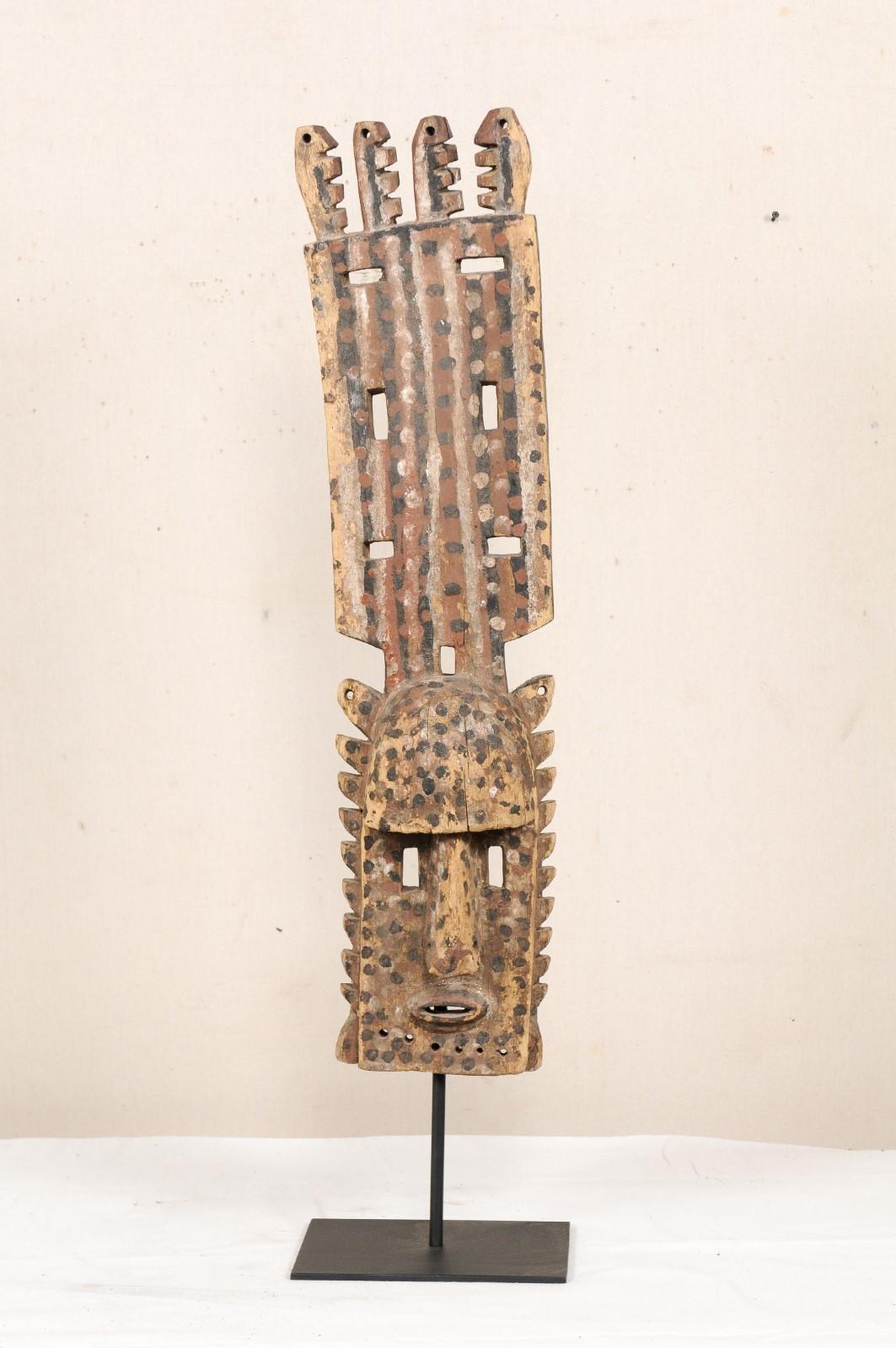 A Dogon Mali dance mask from the early to mid 20th century. This Dogon tribal wooden ceremonial dance mask originates from Mali, West Africa. The mask is carved and features a face with raised head-dress, adorn with pierced triangular-shaped