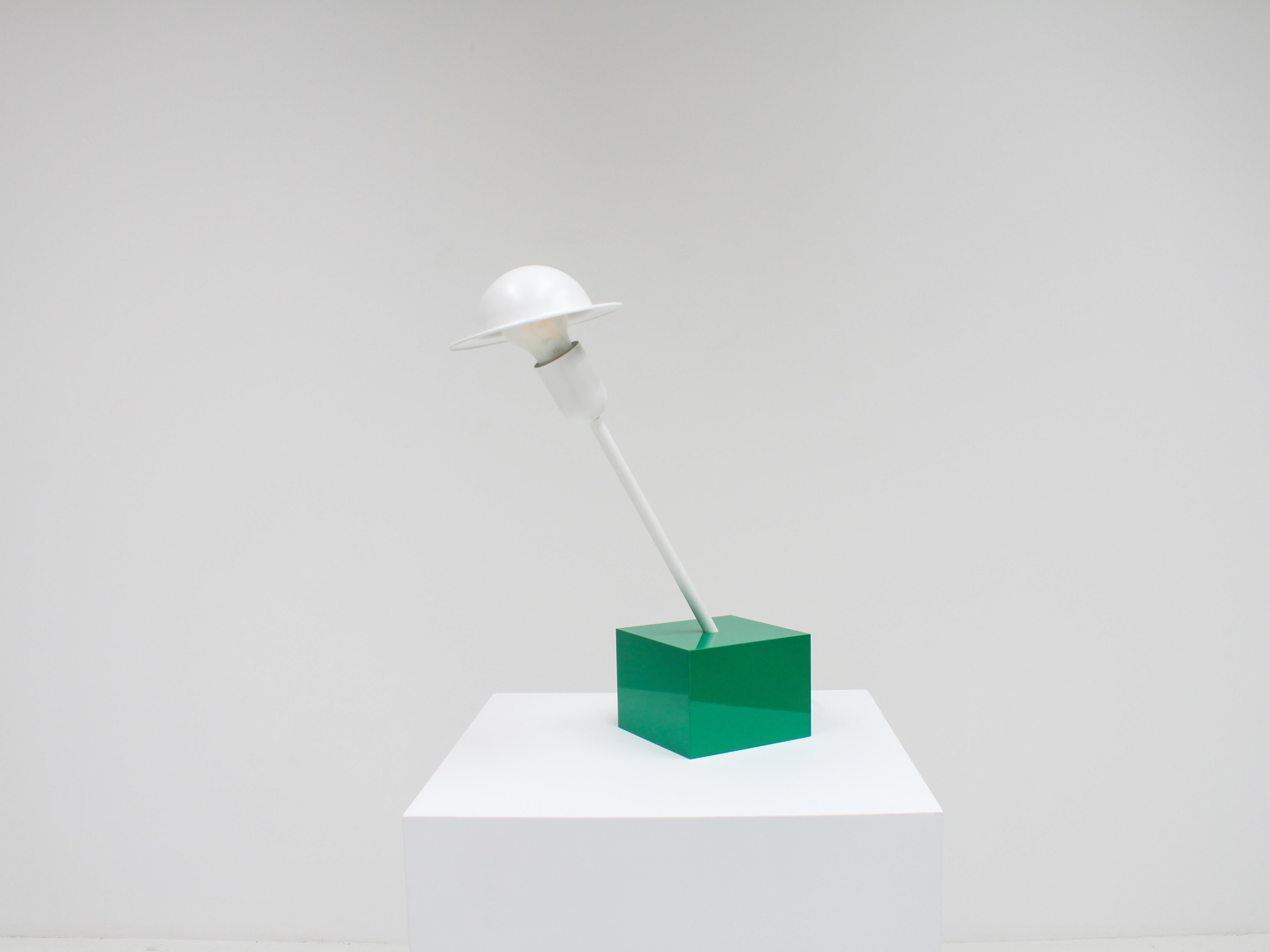 A Don table lamp designed by Ettore Sottsass in 1977. The lamp was manufactured by Stilnovo, Italy, and has a manufacturer’s label.

Consisting of a heavy cubical emerald green base with a white slanted rod and adjustable 'bowler hat'