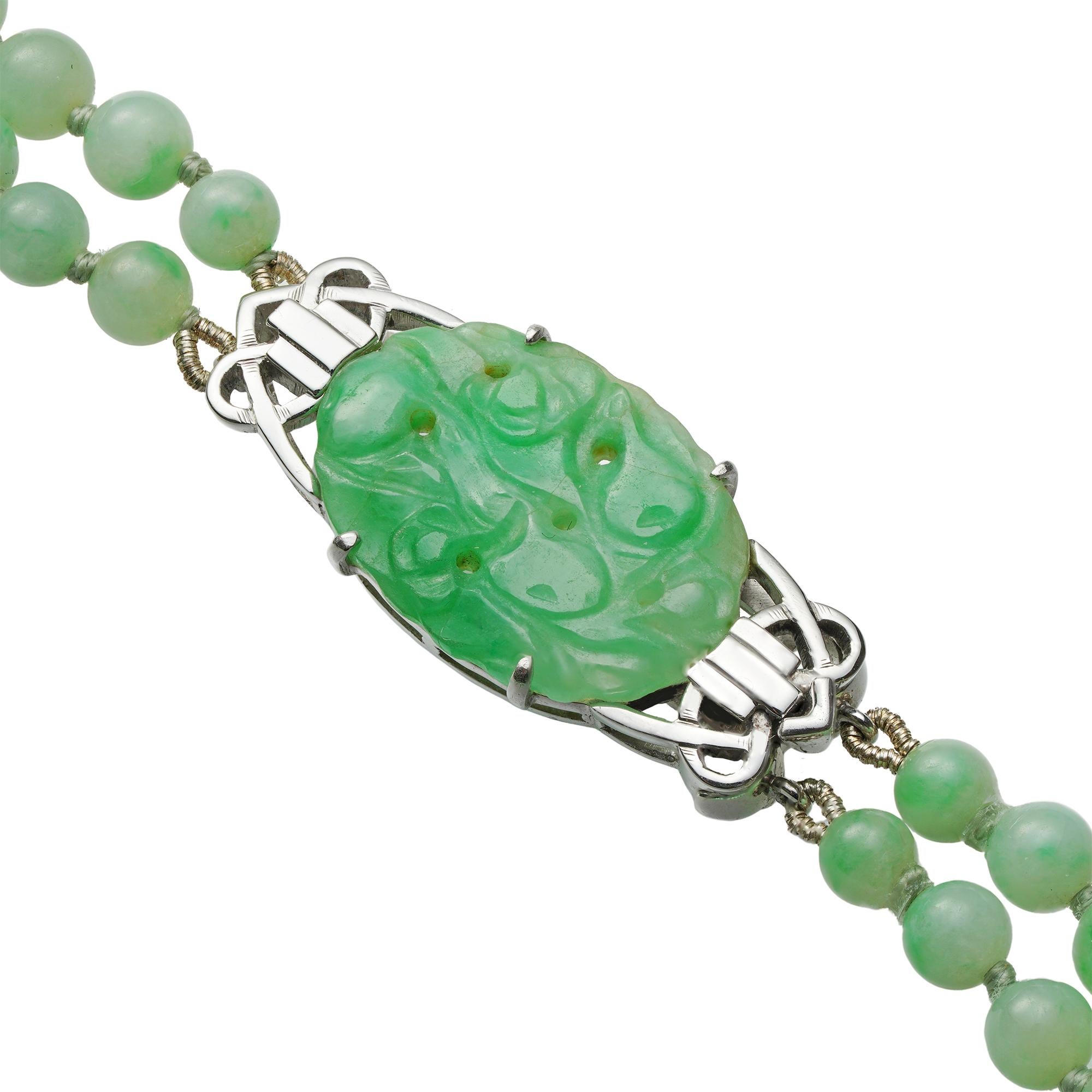 A double-row jade necklace, the one hundred and forty-four beads strung to two rows graduating from the center, their diameter ranging from 4.0mm to 10.0mm, all to a white metal box clasp set with a carved oval-shaped jade plate, circa 1920, the