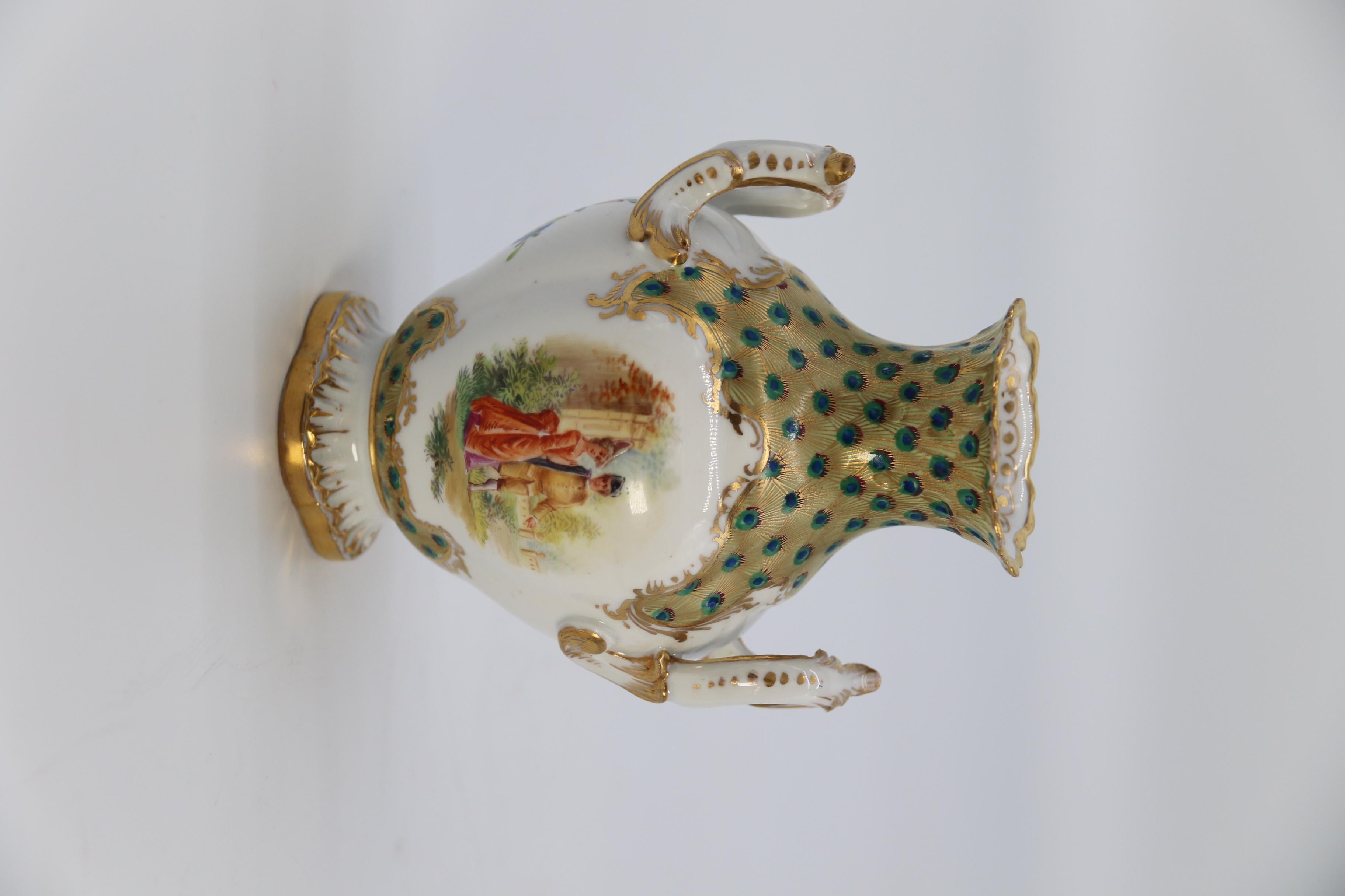 This exceptionally beautiful hand painted vase was made at the Dresden Porcelain Factory in Germany, circa 1900. It is a small twin handled Rocco revival porcelain vase with a most unusual brightly decorated collar of hand painted and gilded peacock
