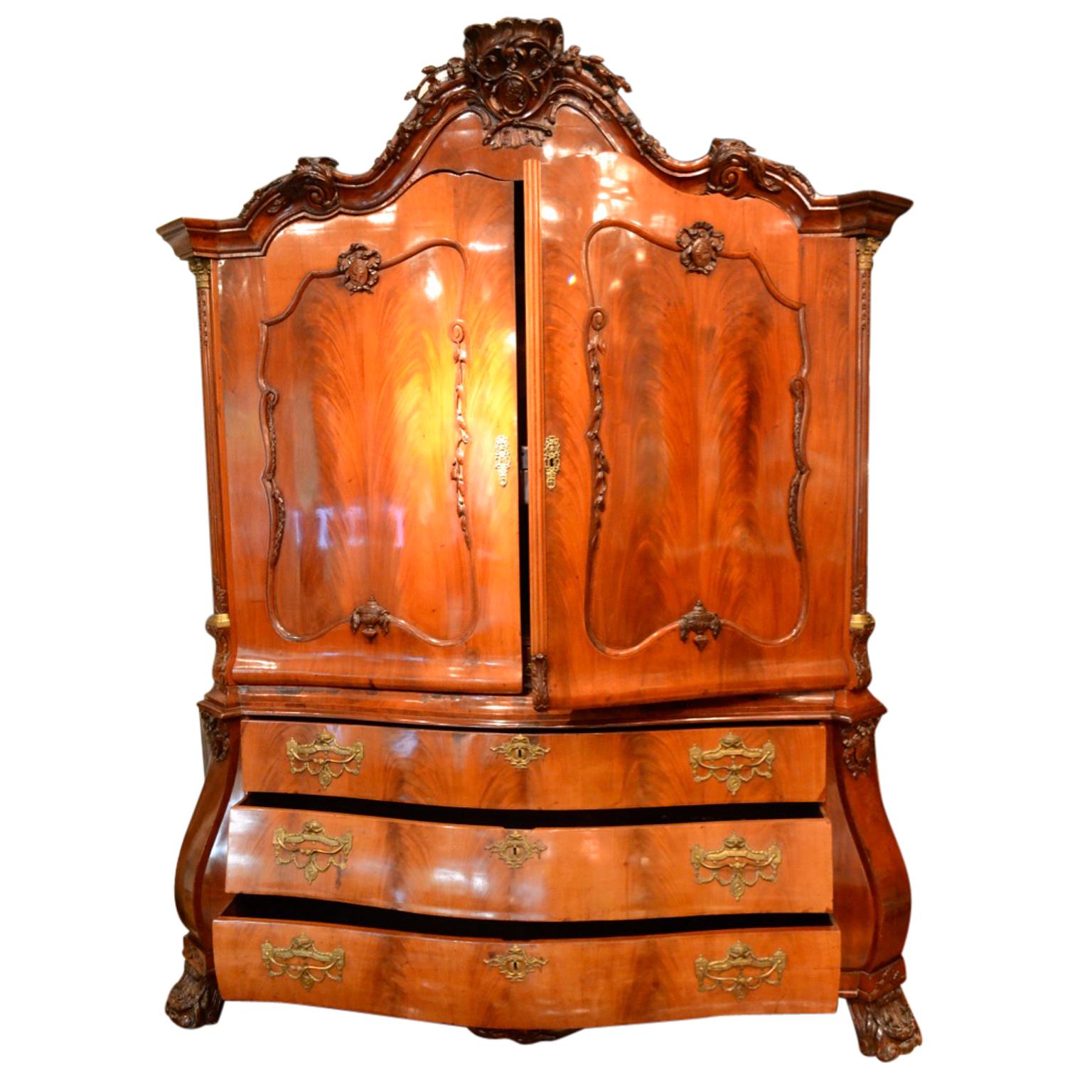 A Louis XV period Dutch mahogany armoire and chest of drawers that in its time would have been used as a linen press. The armoire is topped with a serpentine carved cartouche showing a classical male head in profile wearing a wreath; inset in open