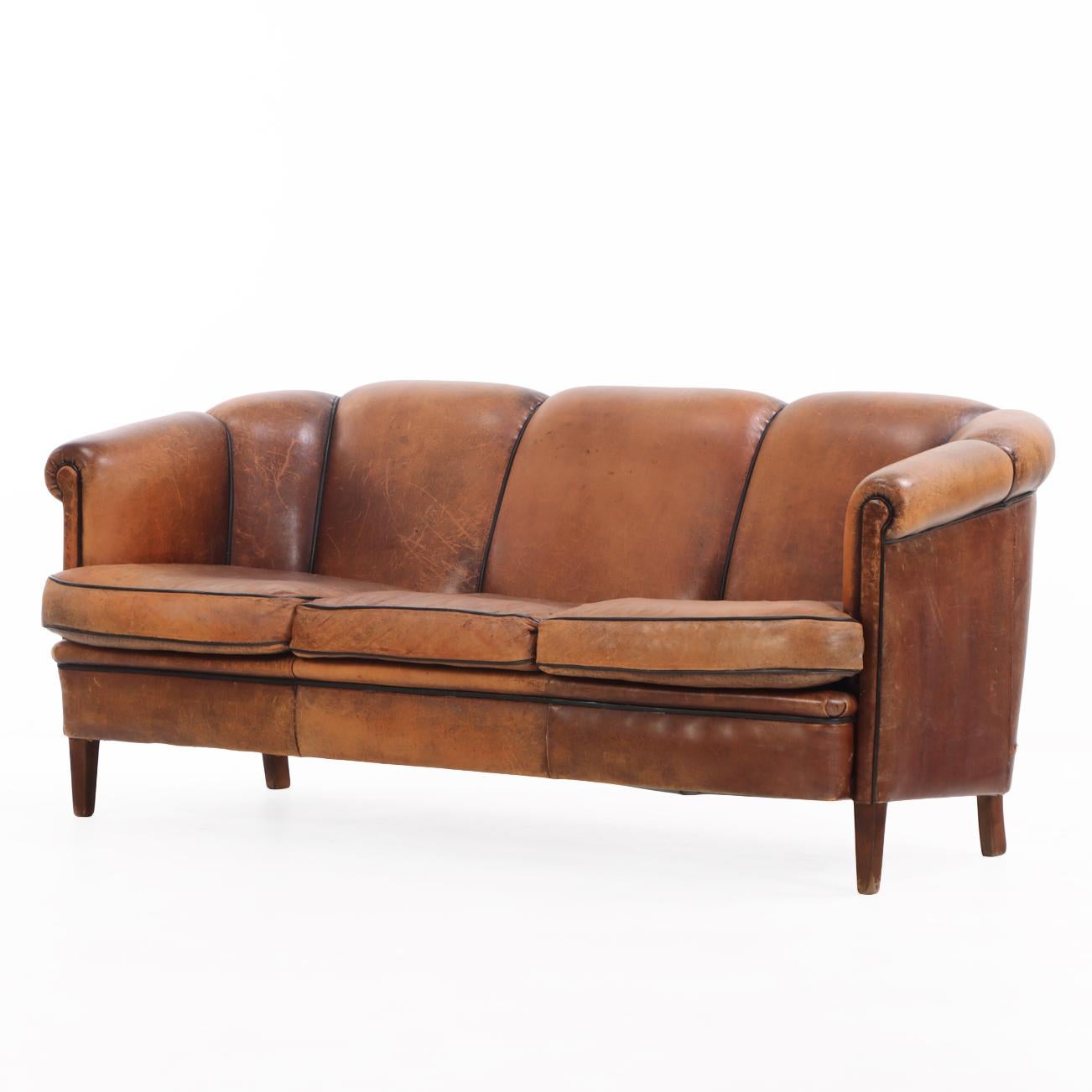 A handsome Dutch leather sofa in the Art Deco style, circa 1960. The three-seat form features gracefully curved back and arms, with rich patinated brown leather upholstery showing a beautiful natural wear and depth of tone. With contrast piping and