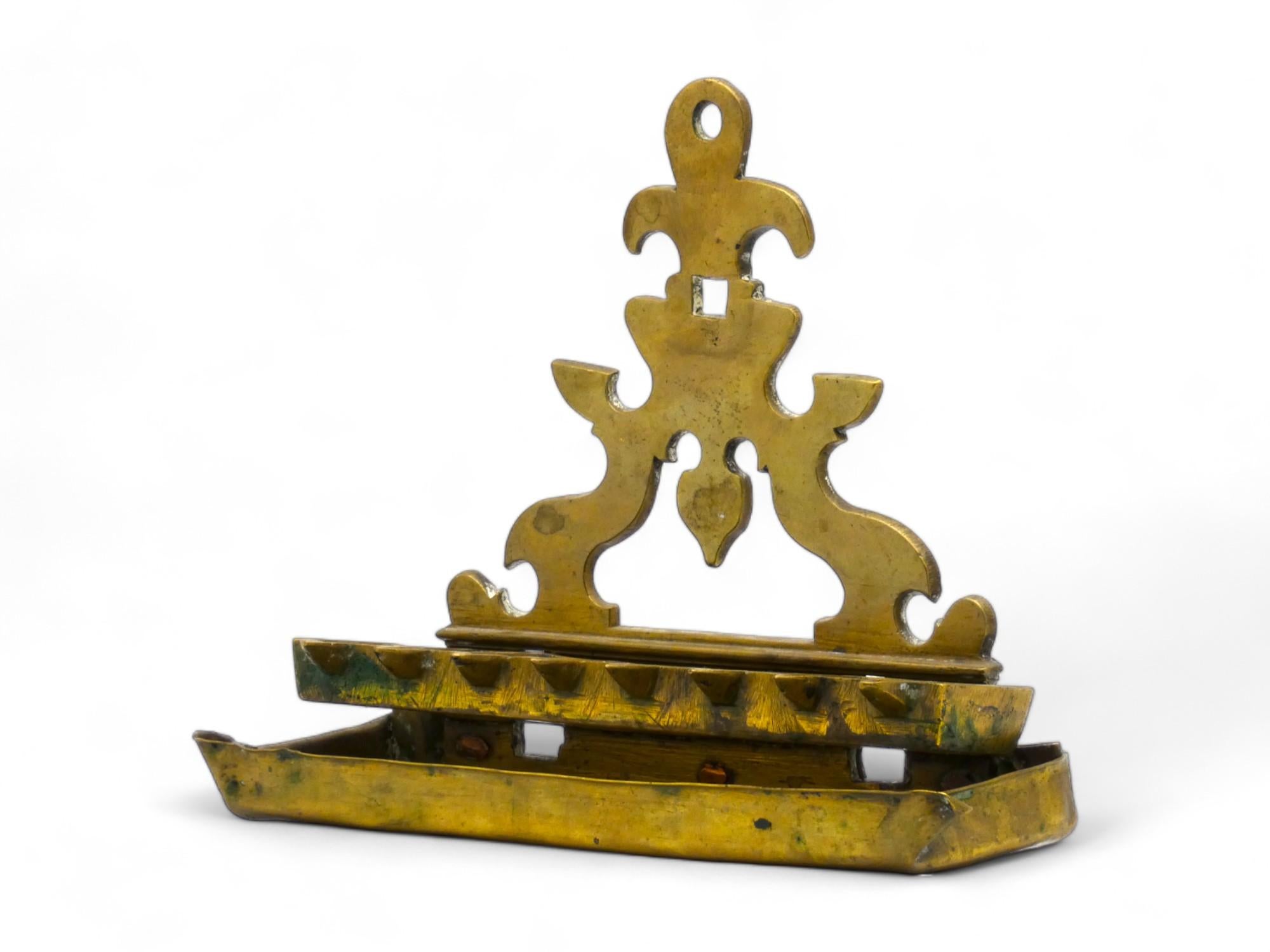 Una lampada Hanukkah olandese in ottone realizzata in stile barocco nel XVIII secolo.

La piastra posteriore triangolare traforata, disegnata quasi a mo' di buco di serratura, sostiene otto profondi recipienti rettangolari per l'olio con beccucci a