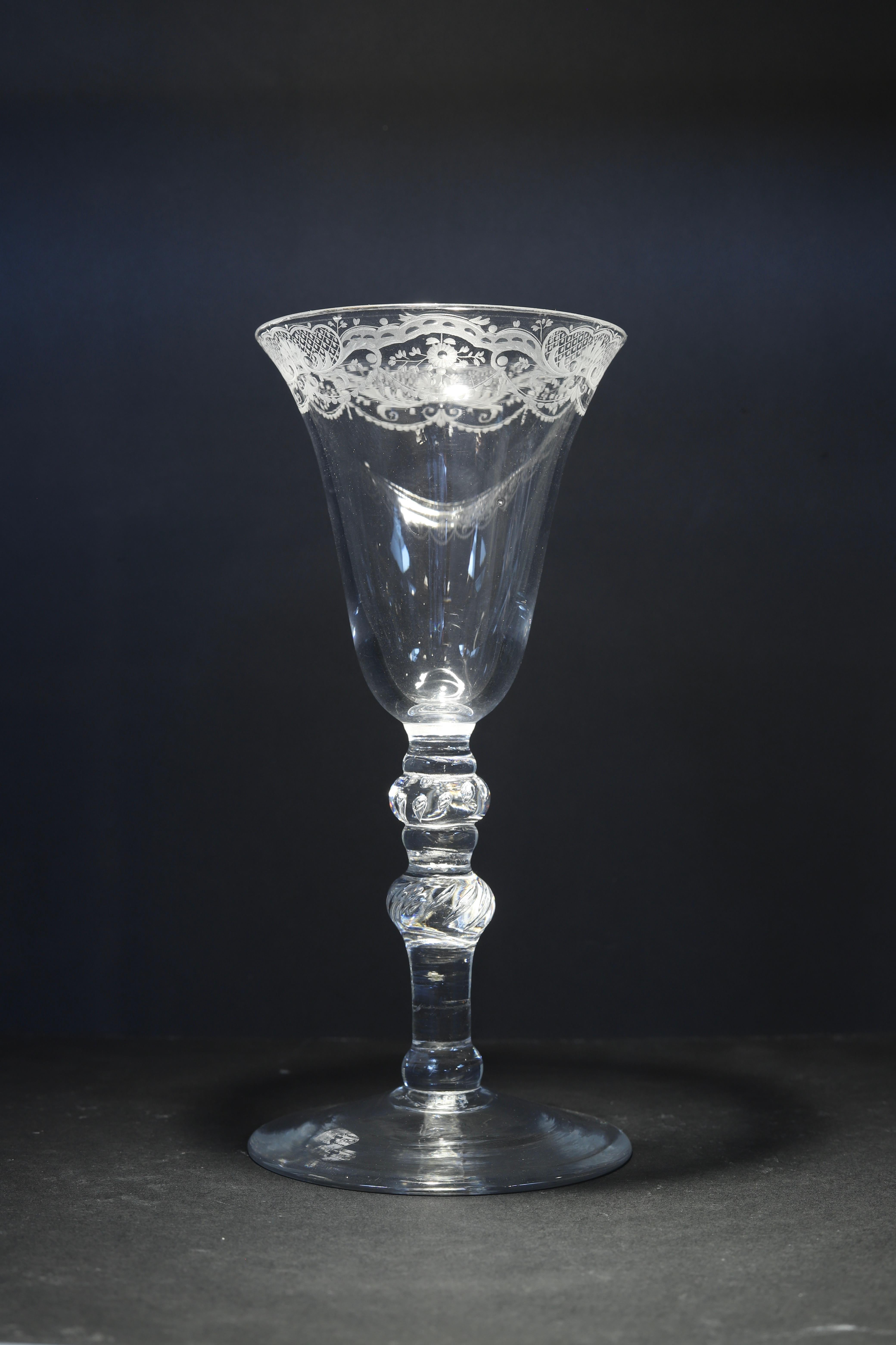 England, Newcastle
Engraving: English or Dutch
Mid 18th century

A heavy baluster Dutch? engraved wine glass with a bell-shaped bowl, the rim decorated with garlands, floral ornaments, and diaper work, the stem with multiple knops, of which two have