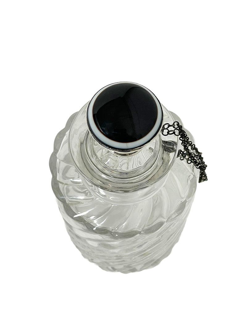 A Dutch glass bottle with silver stopper by Manikus and Verhoef, 1880-1906

A glass bottle with twisted pattern. Around the neck of the bottle a silver collar with chain to which the stopper is attached. The silver is hallmarked with the old