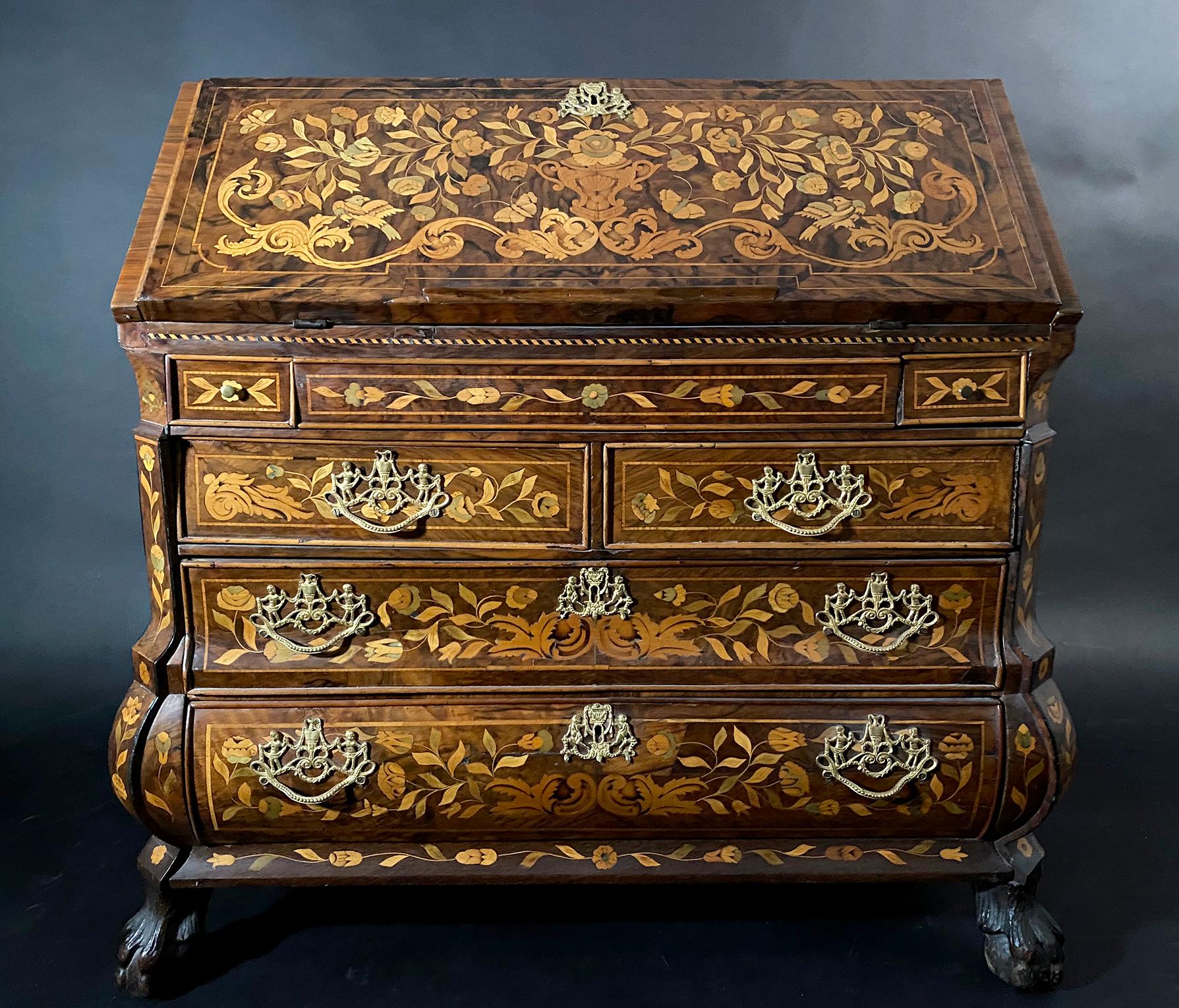 The rectangular top above a drop front revealing an interior writing surface with chubby holes and drawers above a freeze flanked by pencil drawers and four (4) further drawers terminating in lion paw feet. The piece entirely covered in marquetry