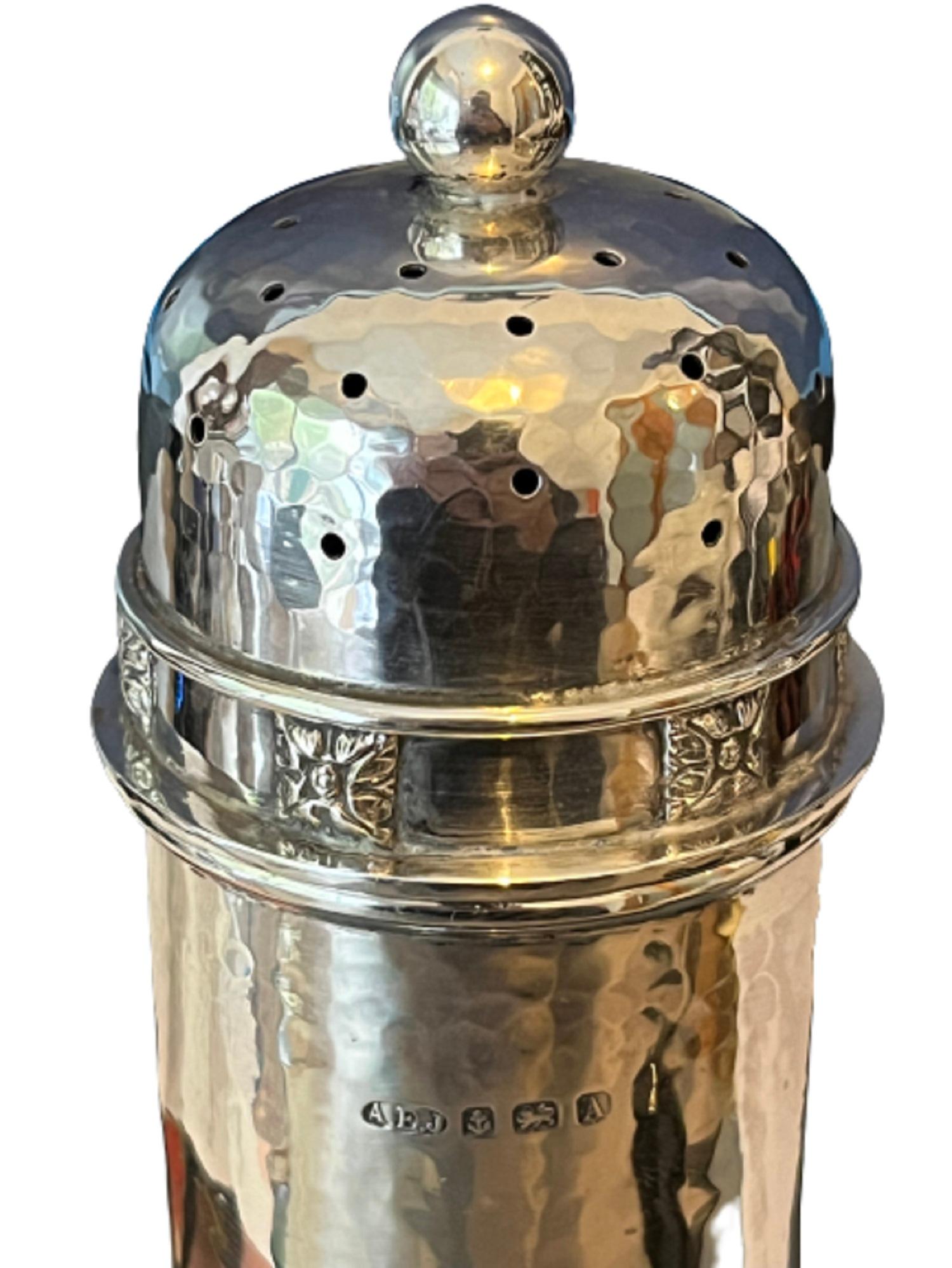 AN ARTS & CRAFTS SILVER SUGAR CASTER, of large size, the body with all-over hand hammered finish, twisted wirework decoration to the base, the detachable pierced cover with a frieze of silver lozenges depicting stylised flowers or leaves.

A.E.