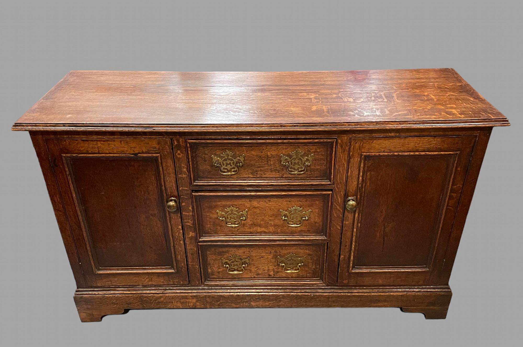 An Early 19th century Oak Dresser Base, the top with a moulded edge with three central drawers with original handles flanked by two cupboards each with a shelf, brass handles on bracket feet.