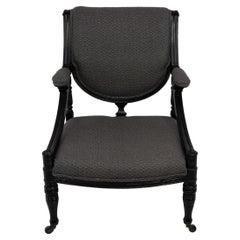 Antique An Aesthetic Movement ebonized & upholstered armchair with sweeping side rails.
