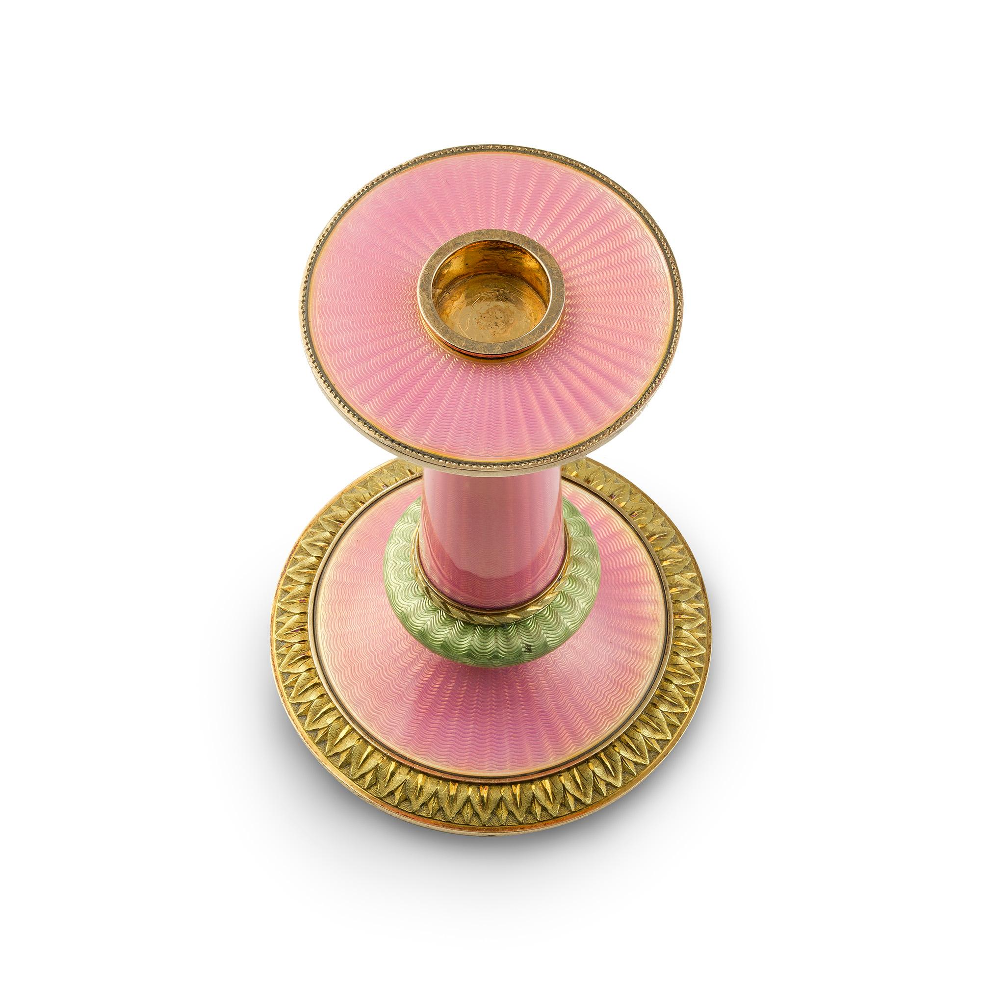 A Faberge pink & green enamel taperstick holder by Faberge', the sconce of translucent pink enamel on an engine turned radiating guilloché ground, the pink column with two green enamel sections within laurel leaf chased yellow border, the circular