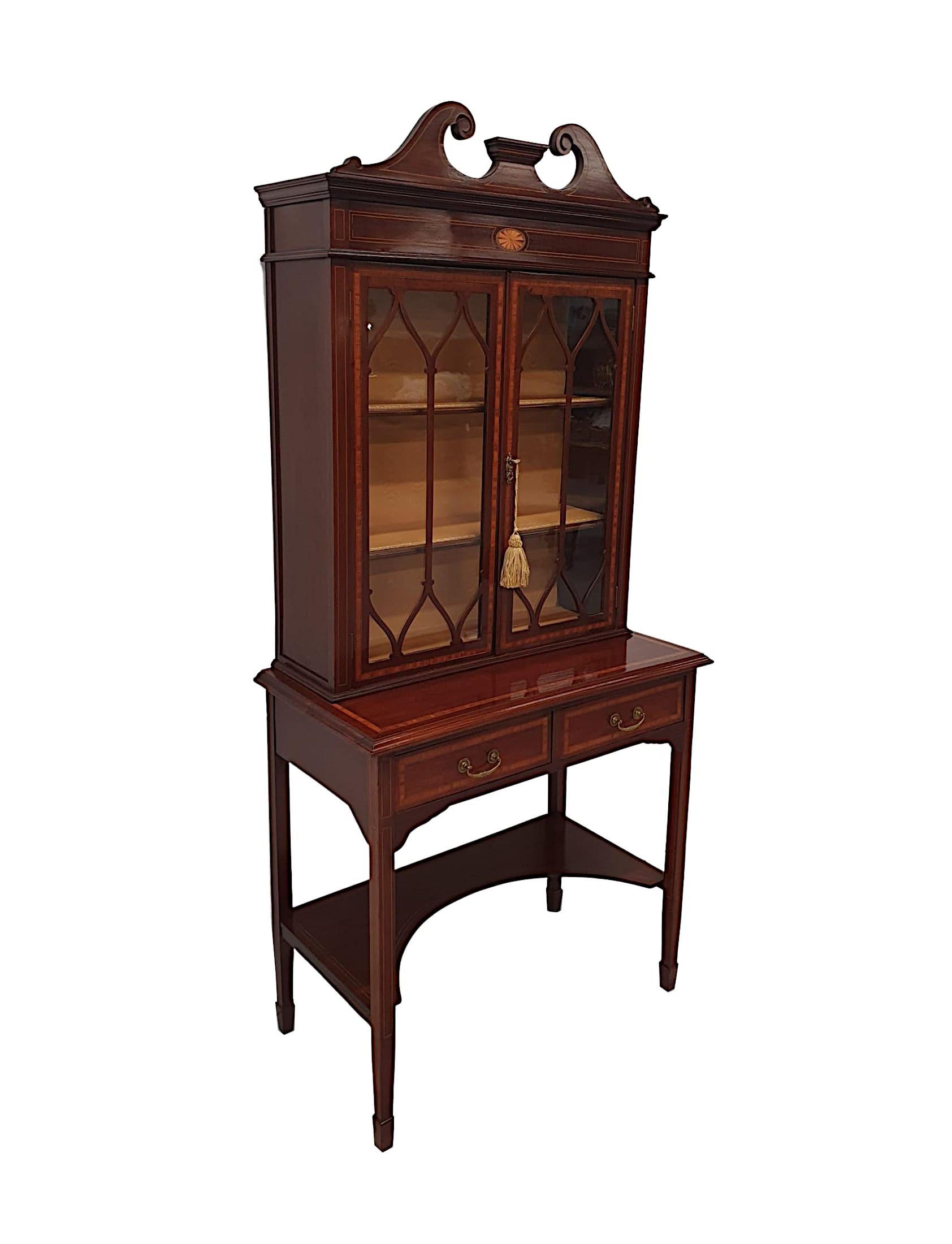A fabulous quality Edwardian mahogany two door display case or bookcase, with gorgeous patination, marquetry detail and fine line inlay throughout. The broken swan neck pediment raised over moulded cornice with a lovely centred marquetry round fan