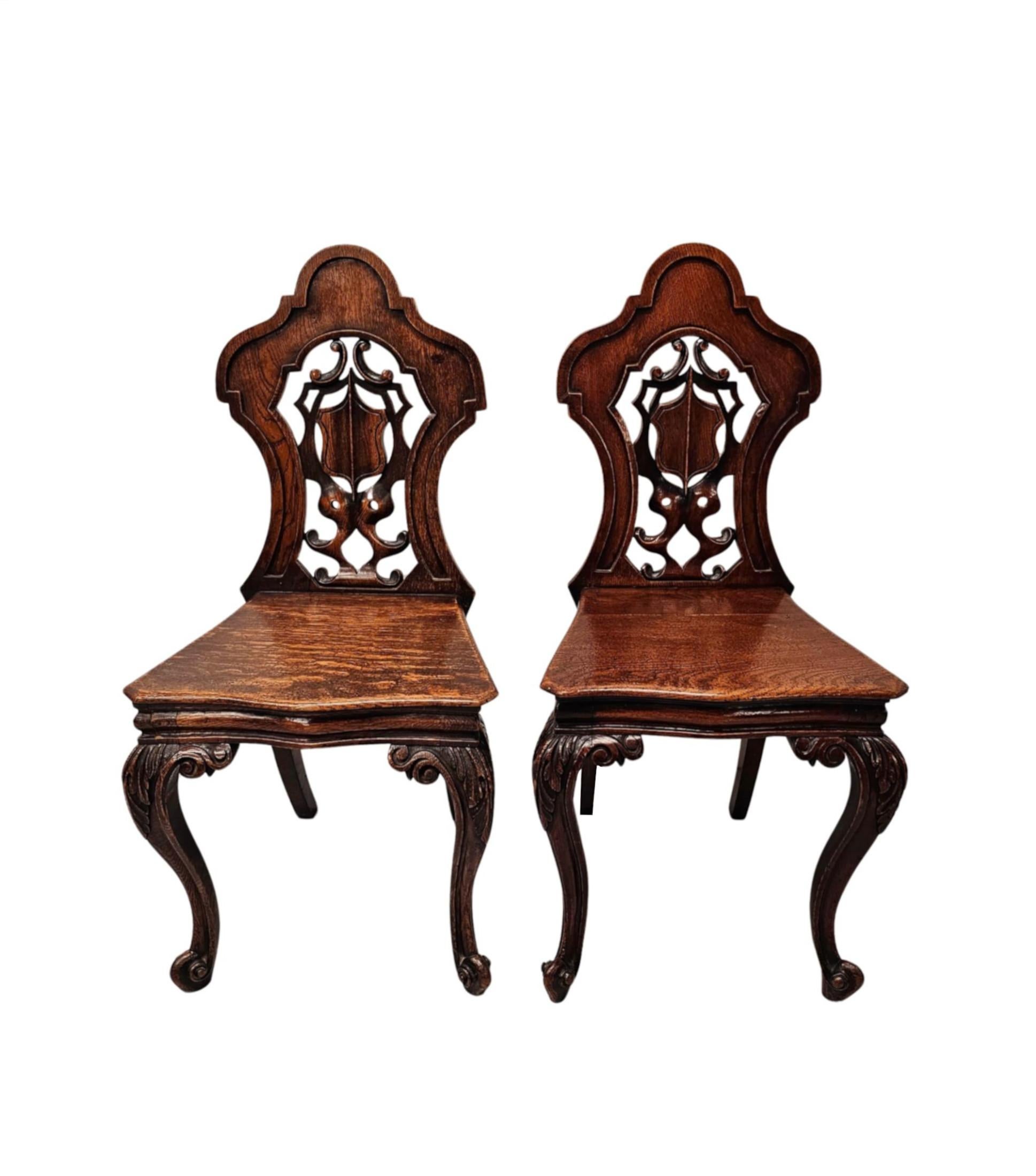 Une fabuleuse paire de chaises de salle en chêne du 19ème siècle de superbe qualité et finement sculptées à la main avec une patine et un grain magnifiquement riches.  Le dos du bouclier, bien figuré, lambrissé et percé, est orné de magnifiques