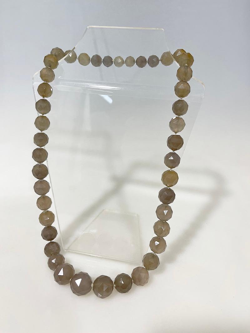Collier de perles à facettes 

43 boules de pierre facettées transparentes avec des tons gris laiteux et brun clair, variant de la taille 2 cm en diagonale à 1 cm en diagonale, enfilées et nouées sur du fil régulier. 
Veuillez regarder les photos