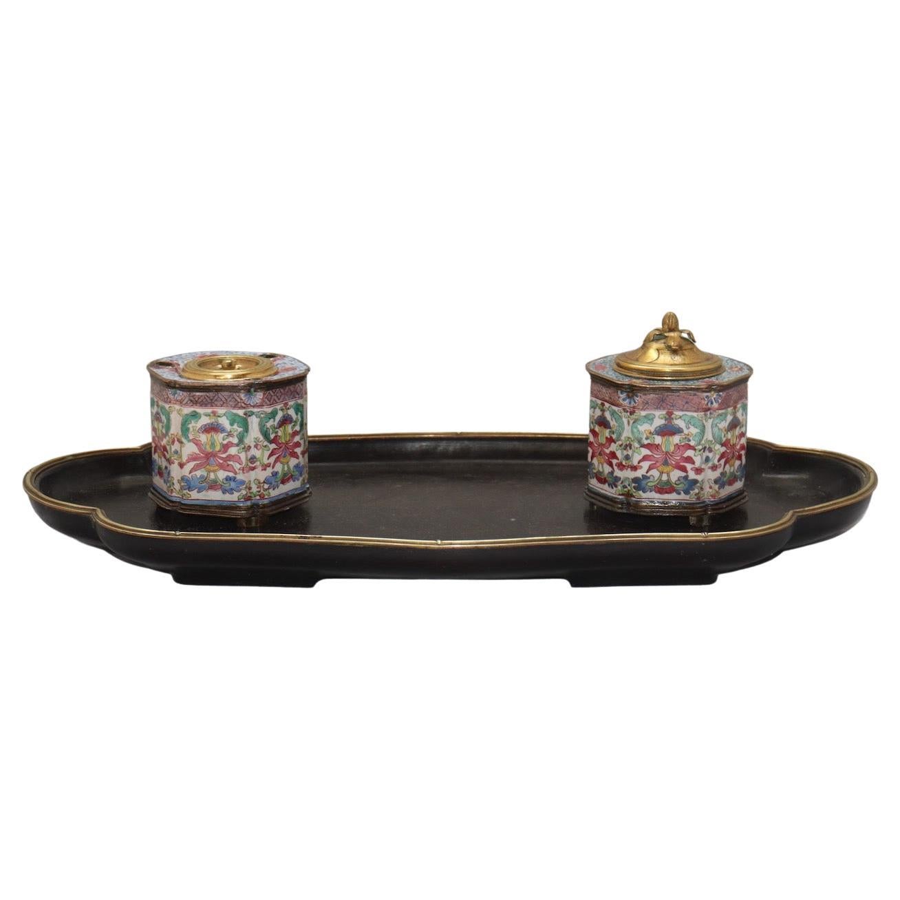 A Famille Rose Painted Enamel inkwell set Qianlong Period (1736-1795) by l’Escalier de Cristal

It consists of a fretworked tray with raised edges in blackened wood surrounded by a fine gilded bronze ring, on which rests two Famille Rose Qianlong