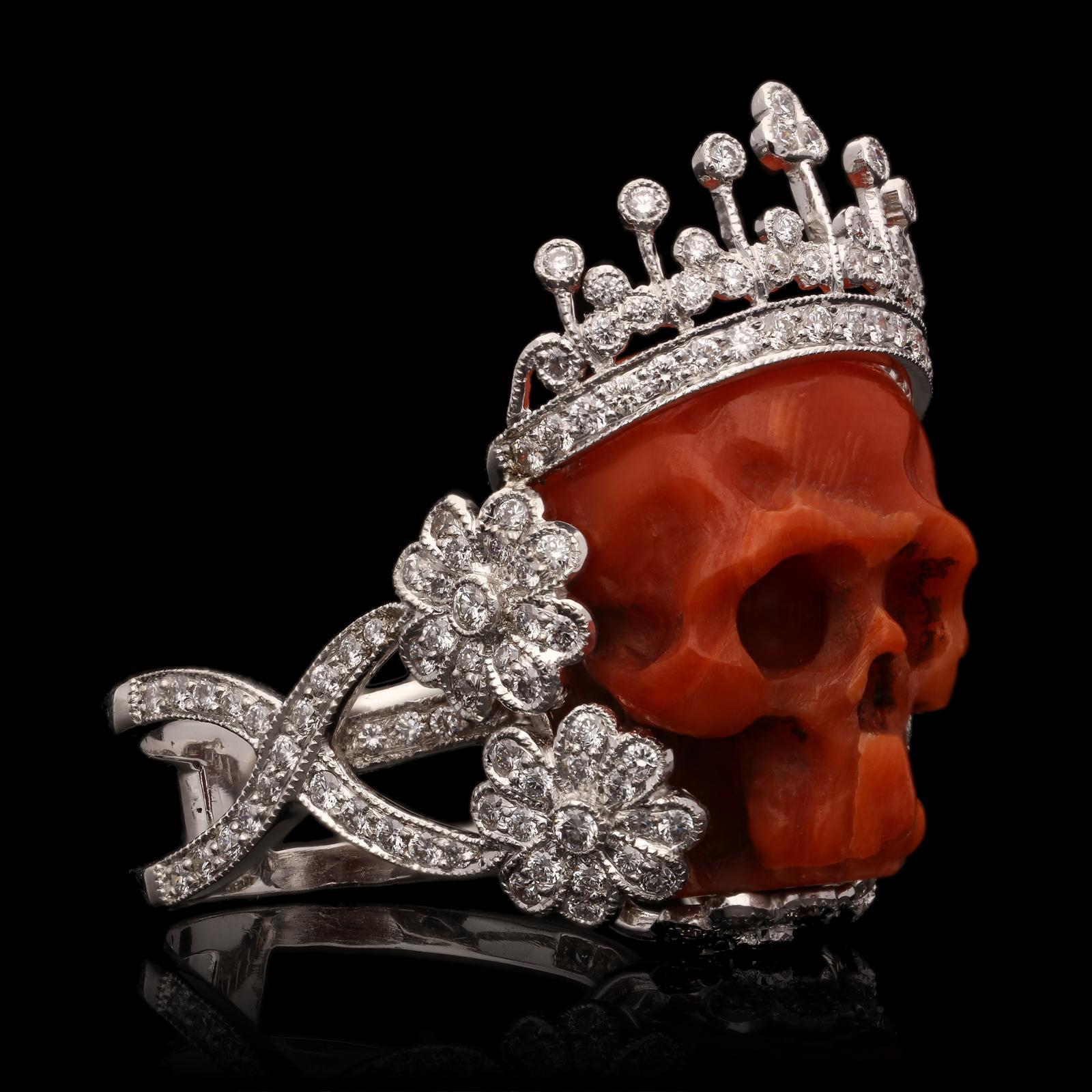 A bold and fantastical coral and diamond ring by Lydia Courteille c.2000, the carved coral skull wearing an 18ct white gold crown set with round brilliant diamonds and around the sides of the face and underneath the chin there are five flower motifs