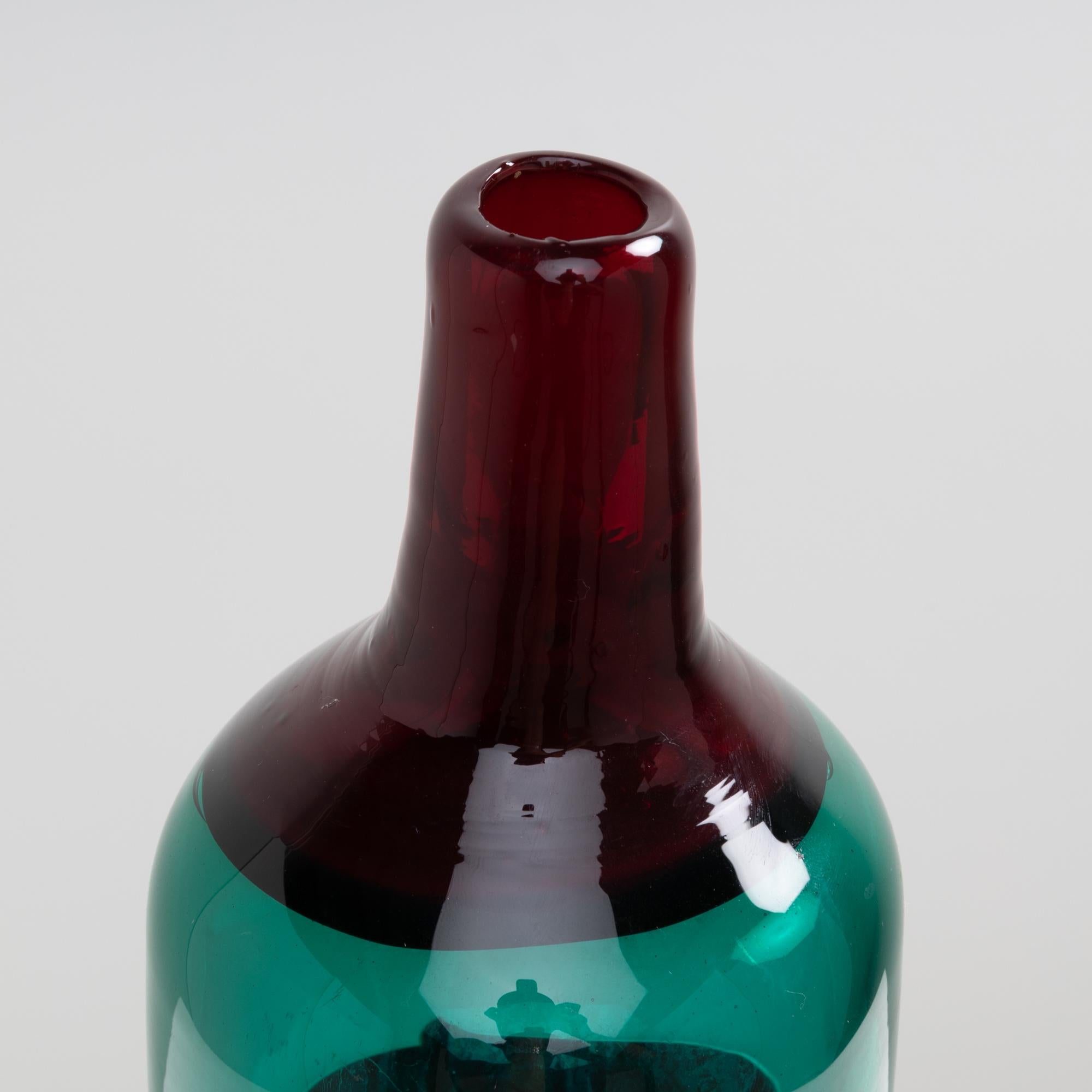 Large green blown glass bottle vase decorated with two hot applied red bands. 
The collar consists of a layer of translucent red glass which is itself different from the glass used for the body of the vase which have a white interior. 

