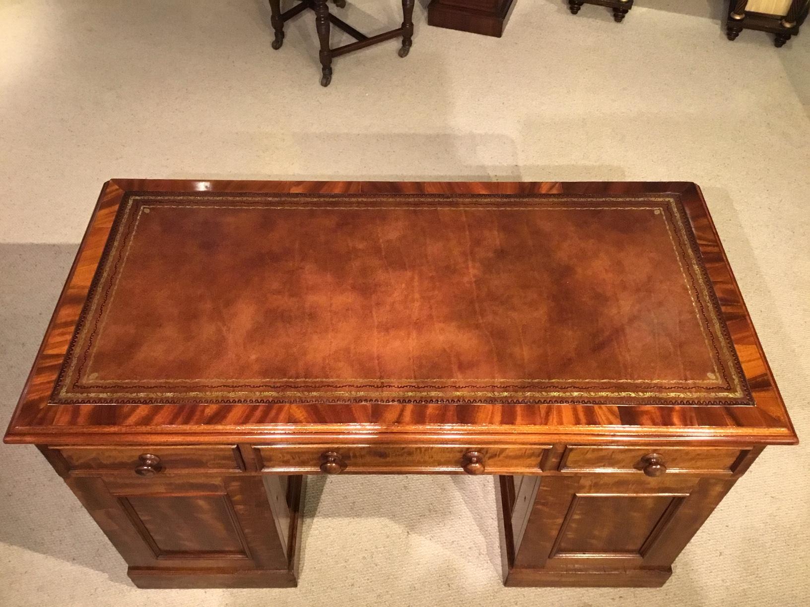 A figured mahogany Victorian period antique writing desk. Having a rectangular top with a tan inset leather writing surface with blind and gilt tooled detail, cross banded in mahogany and with a moulded edge. With an arrangement of three drawers and