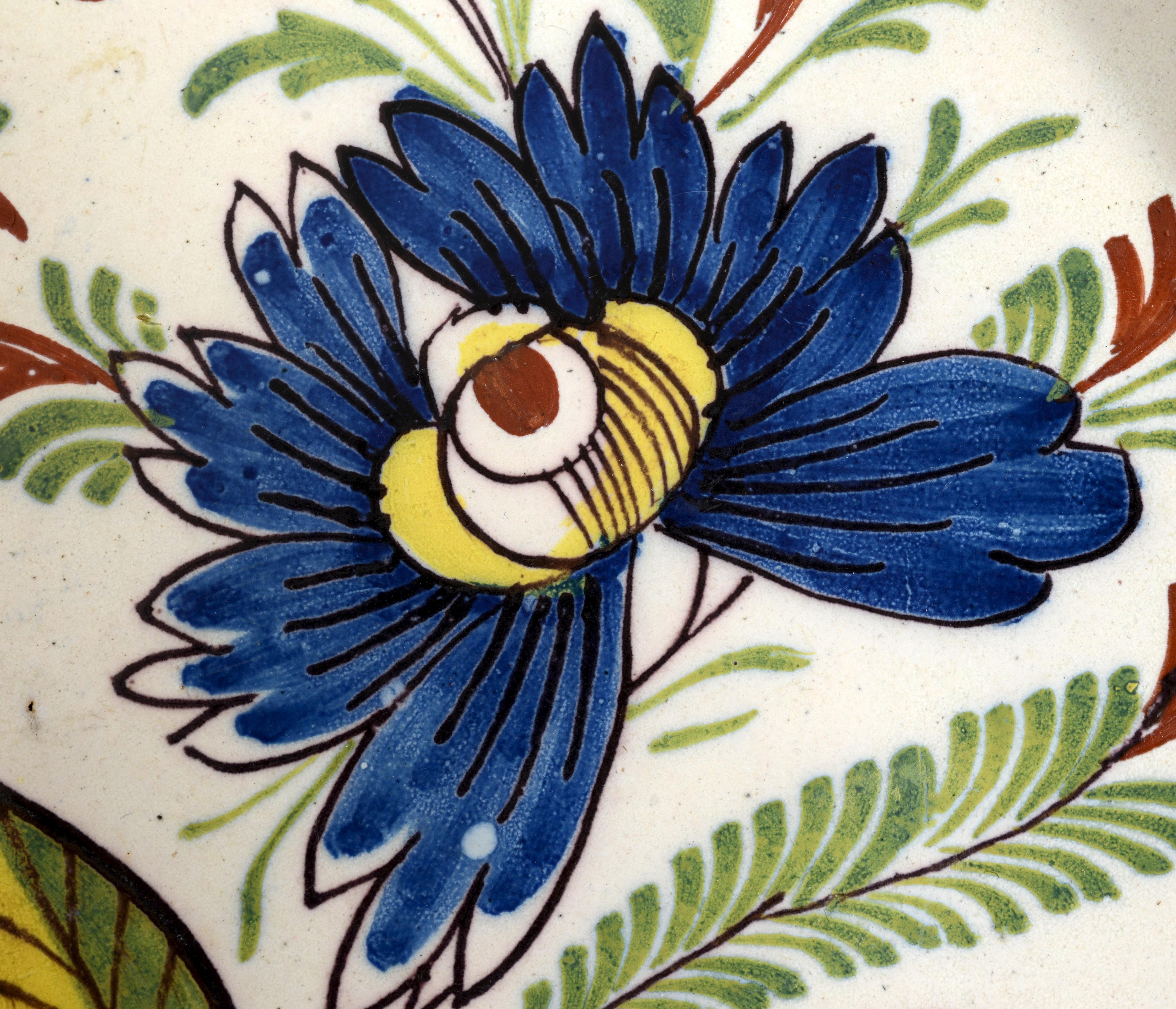 A fine 18th c Dutch Polychrome painted delft charger, decorated with vibrantly colored stylized tulips and flowers painted in manganese, green, yellow and blue. The sloped rim is painted with flowers and leaves. The center of the dished charger is