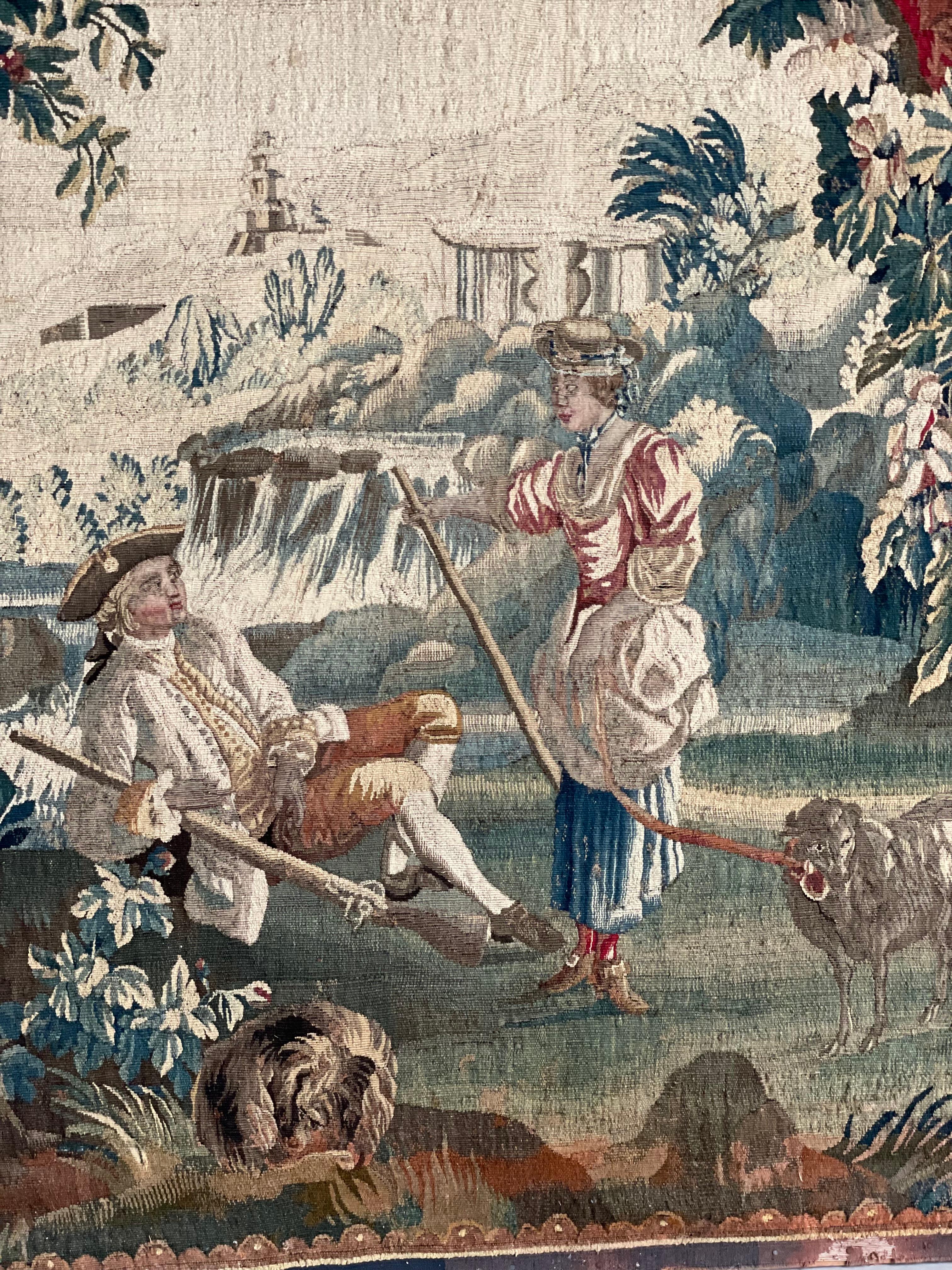 A fine 18th-century Aubusson pastoral tapestry depicting a romantic tryst between a hunter and a shepherdess in a typically rural and architectural-themed landscape. The tapestry is in good general condition, showing some restoration on the lower