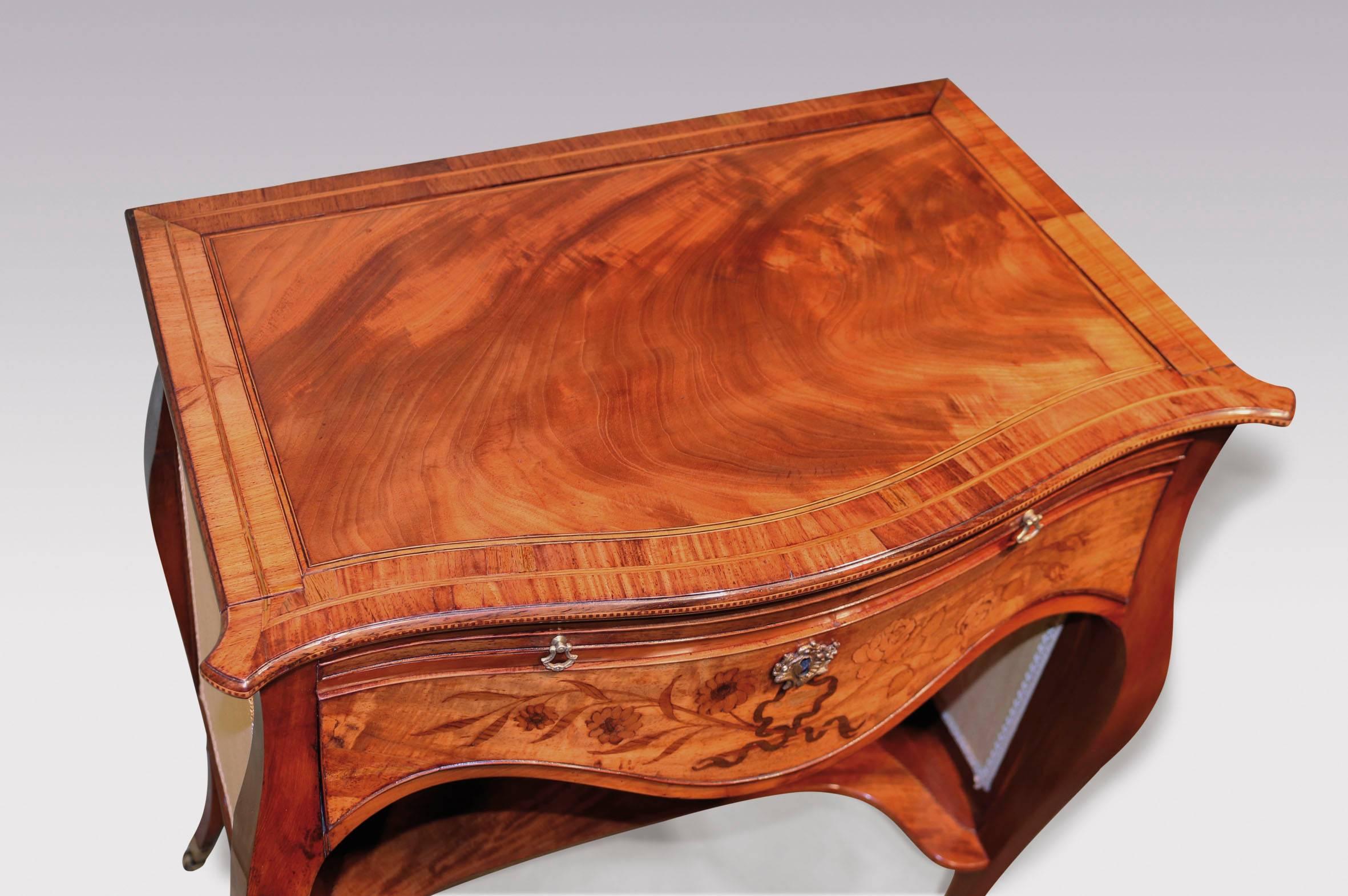 A late 18th century ‘French Hepplewhite’ figured mahogany ladies writing table of serpentine form, having boxwood and ebony strung tulipwood crossbanded top with chequered inlaid edge. The table with three lift up slides centered with marquetry