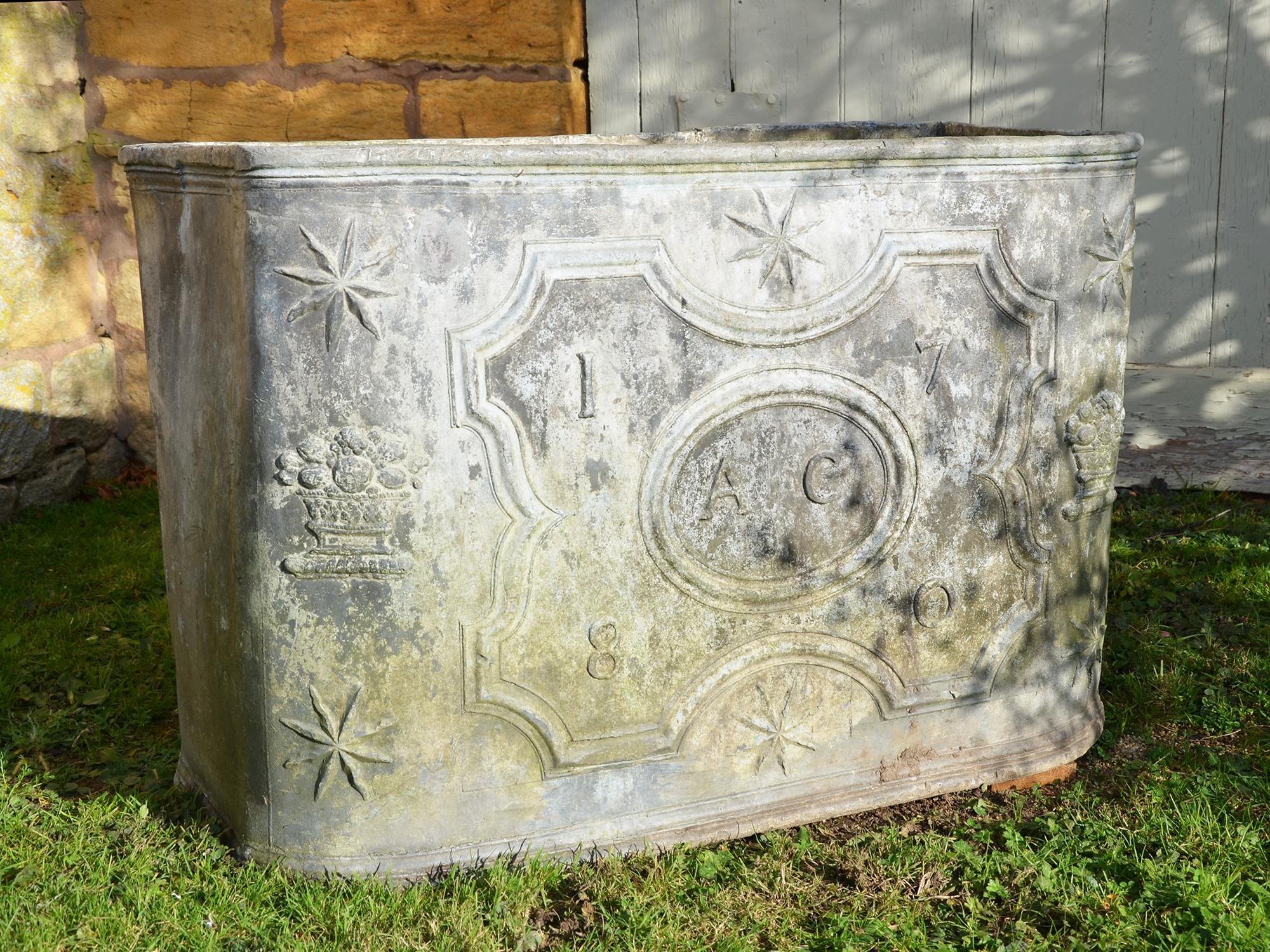 A fine 18th century lead cistern of rectangular form having decoration to the front section in the form of sunburst and flowers in a lattice-work bowl, surrounding a parterre design moulding within which are the initials A C in an oval moulding and