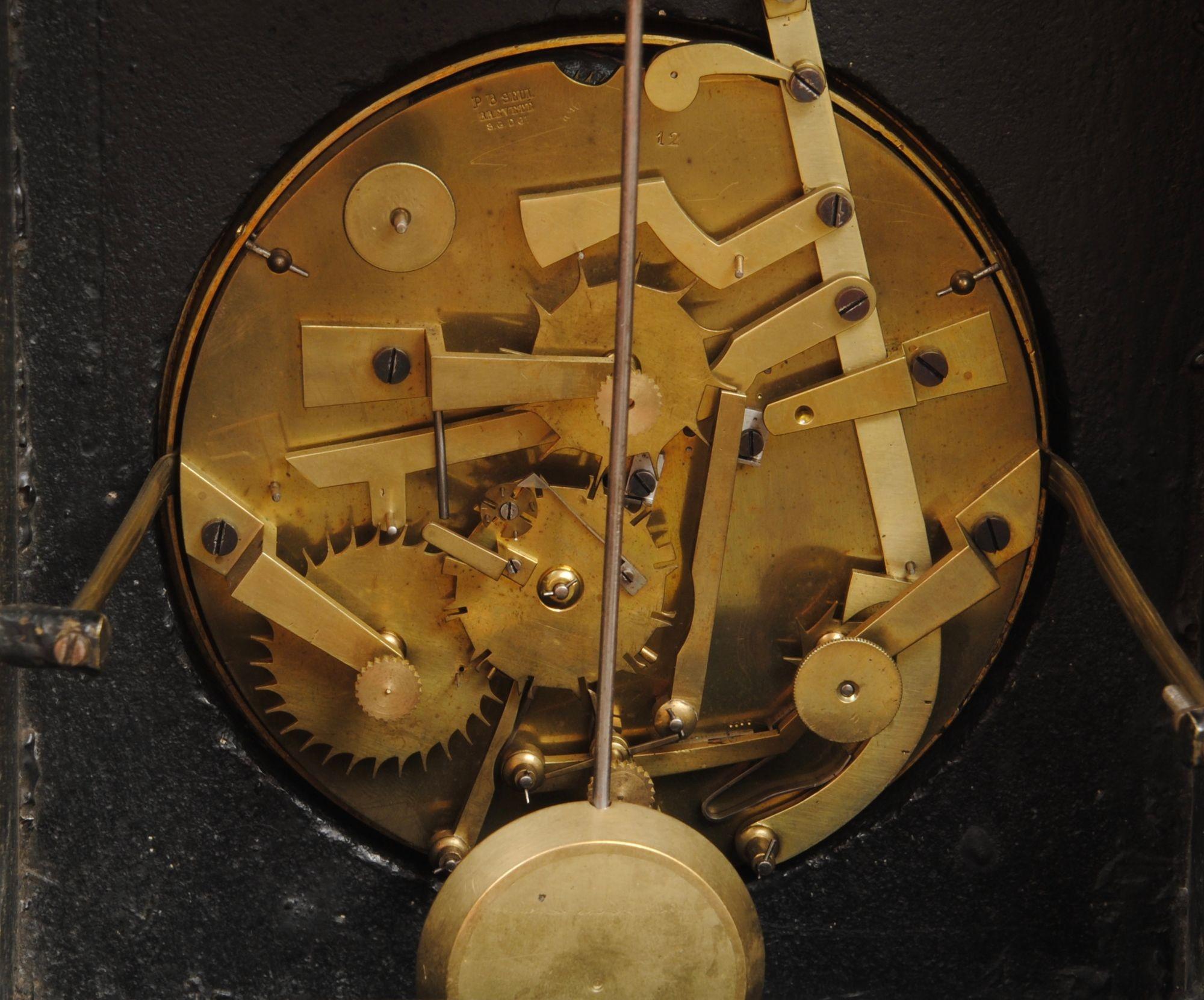 Pendule à phase de lune perpétuelle en ardoise belge avec échappement en brocot visible sur le cadran émaillé.

Le cadran en émail du calendrier est magnifiquement peint de jeunes filles. Les deux cadrans sont enchâssés dans une plaque en bronze