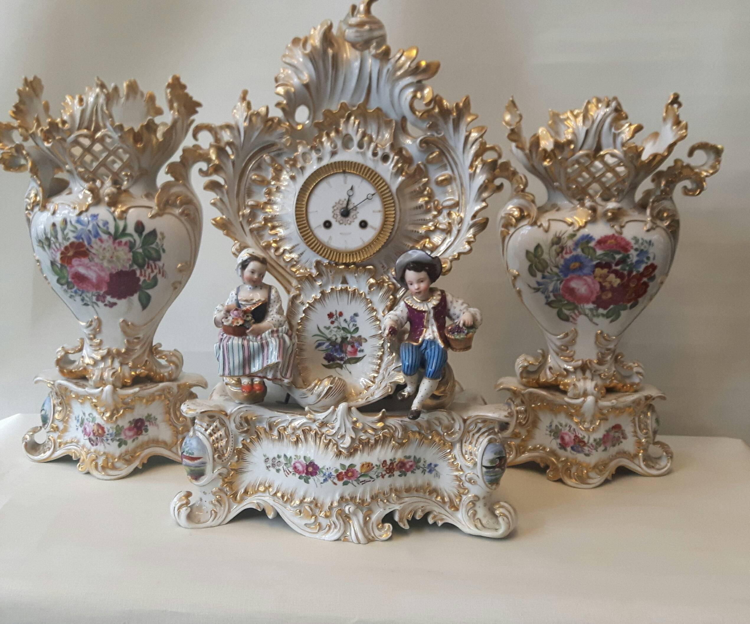 Élégante garniture rococo de Jacob Petit, Paris, vers 1860. L'horloge est minutieusement peinte à la main avec des cartouches de fleurs, tout comme les vases assortis, et une paire de figurines de style Meissen, représentant des jardiniers, orne le