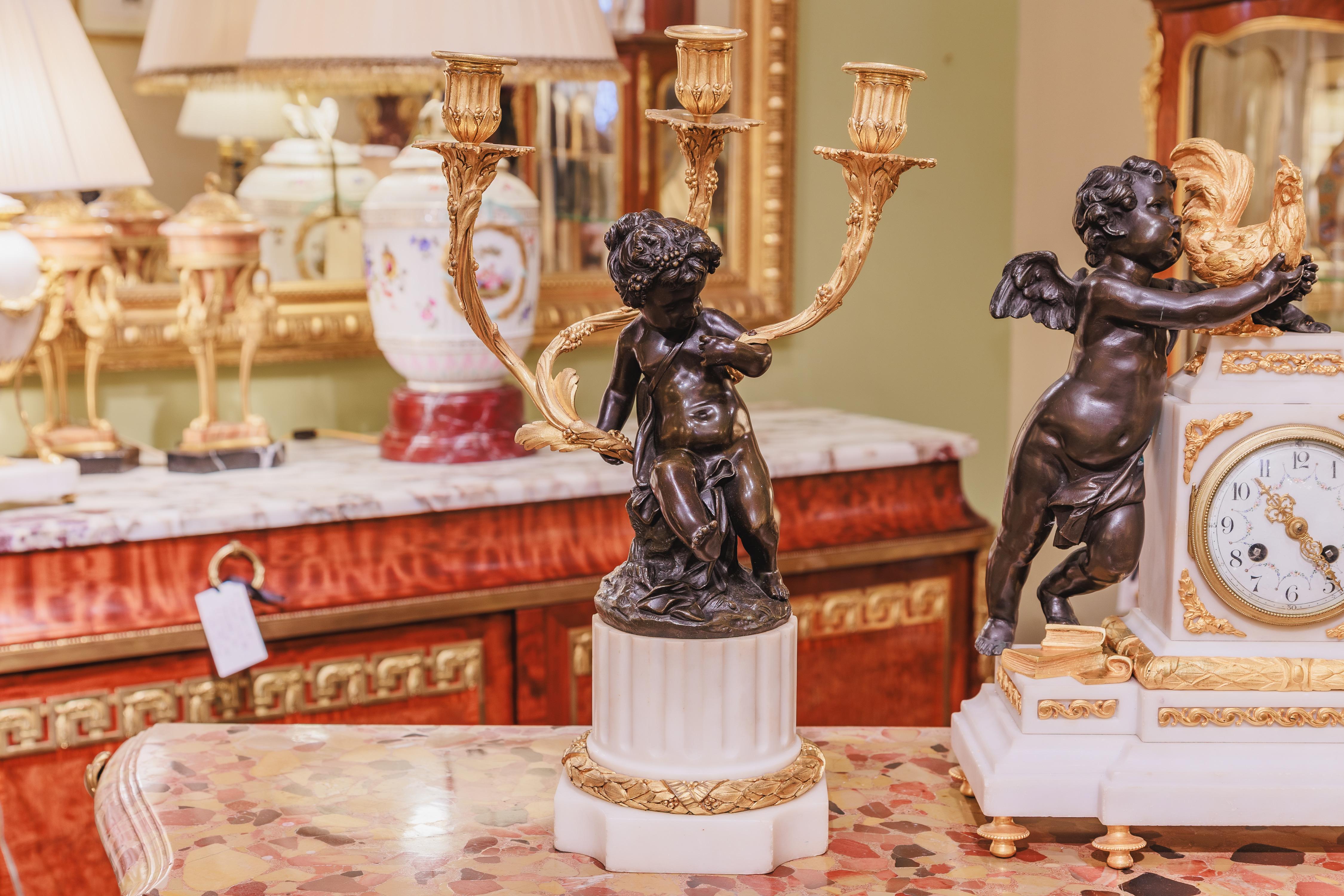 Raffinato orologio francese del XIX secolo in marmo di Carrera e bronzo dorato con cherubino. Set di tre pezzi con una coppia di candelabri e un orologio. L'orologio ha un cherubino in bronzo patinato che tiene in mano un gallo.