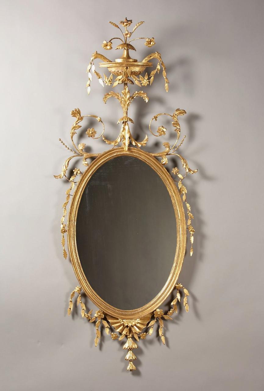 An American giltwood oval mirror having an urn finial with floral spray surmounted by two bird heads and flanked b y stylized vines and foliate carved pendants. Micro-analysis identifies the primary wood as white pine, indigenous to North America. A