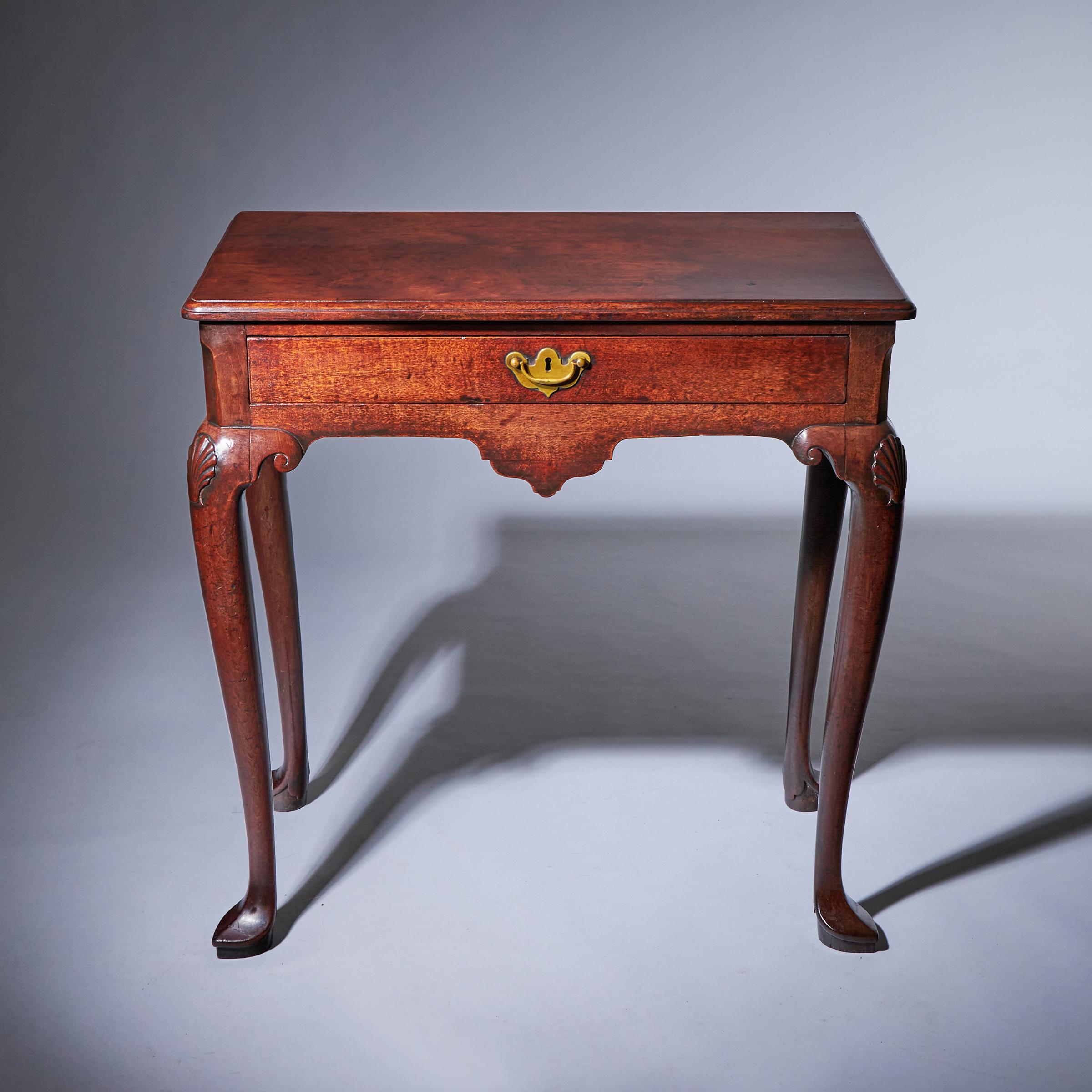 The moulded edge top sits over a canted frieze fitted with a long drawer finely lined in oak retaining original hardware above a similarly conforming shaped central apron. Raised on cabriole legs shell carved to the face and eared, each terminating