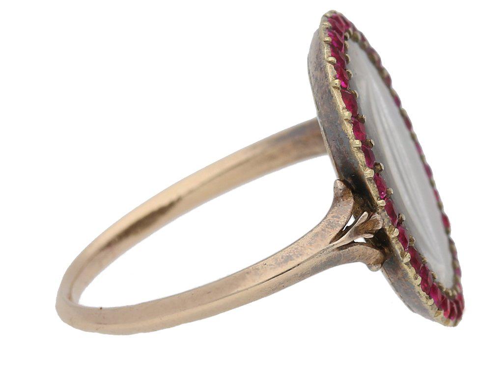 Georgian hair and ruby memorial ring. Set with a border of thirty two cushion shape French cut natural enhanced rubies in closed back grain settings with a combined approximate weight of 1.00 carats, encircling an oval crystal plaque covering an