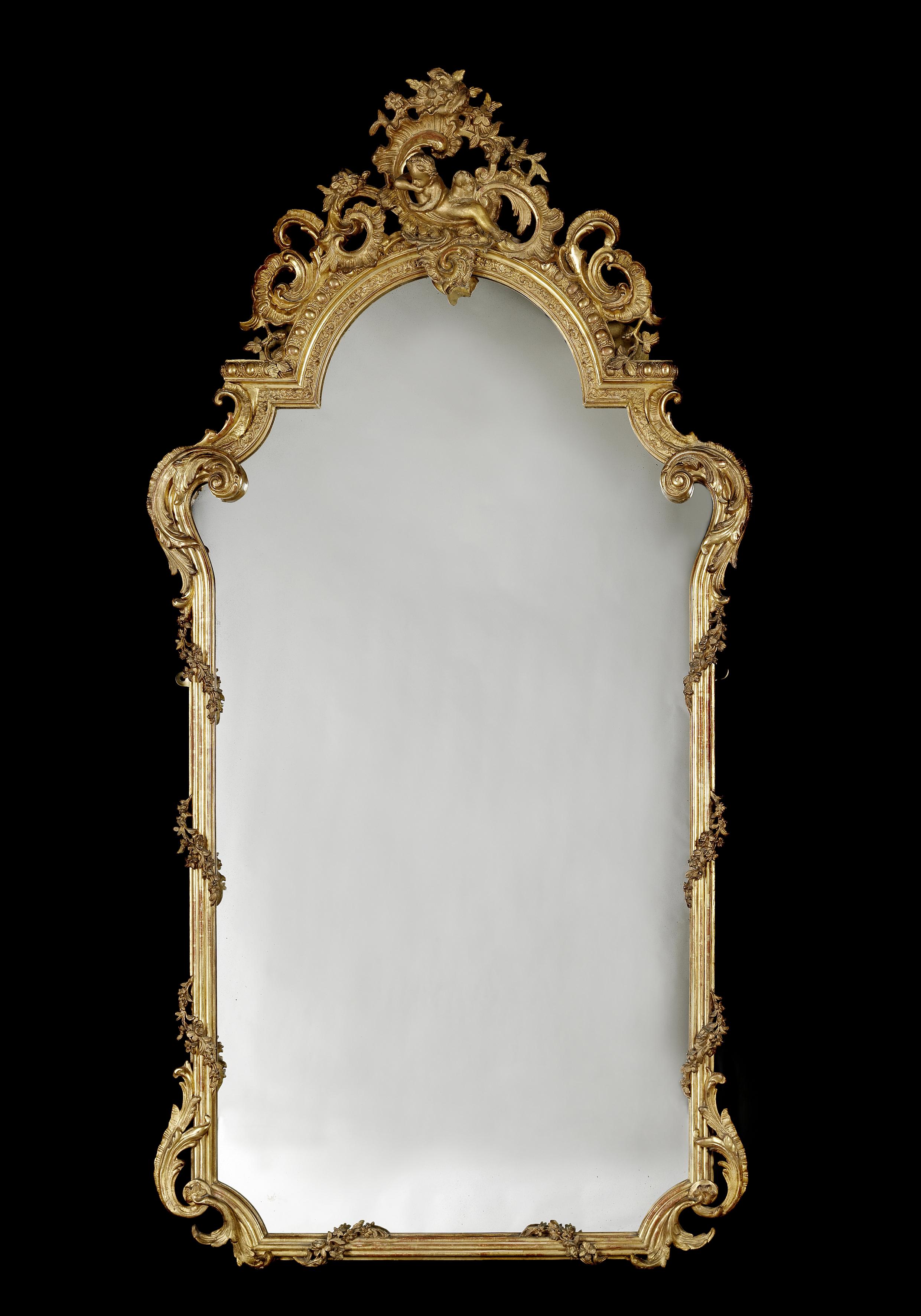 A fine and tall Louis XV style carved giltwood mirror. 

French, circa 1870.

This very finely carved mirror has an arched cresting expressively carved with acanthus ‘C’-Scrolls and rock roses centred by a reclining putti. The reeded uprights
