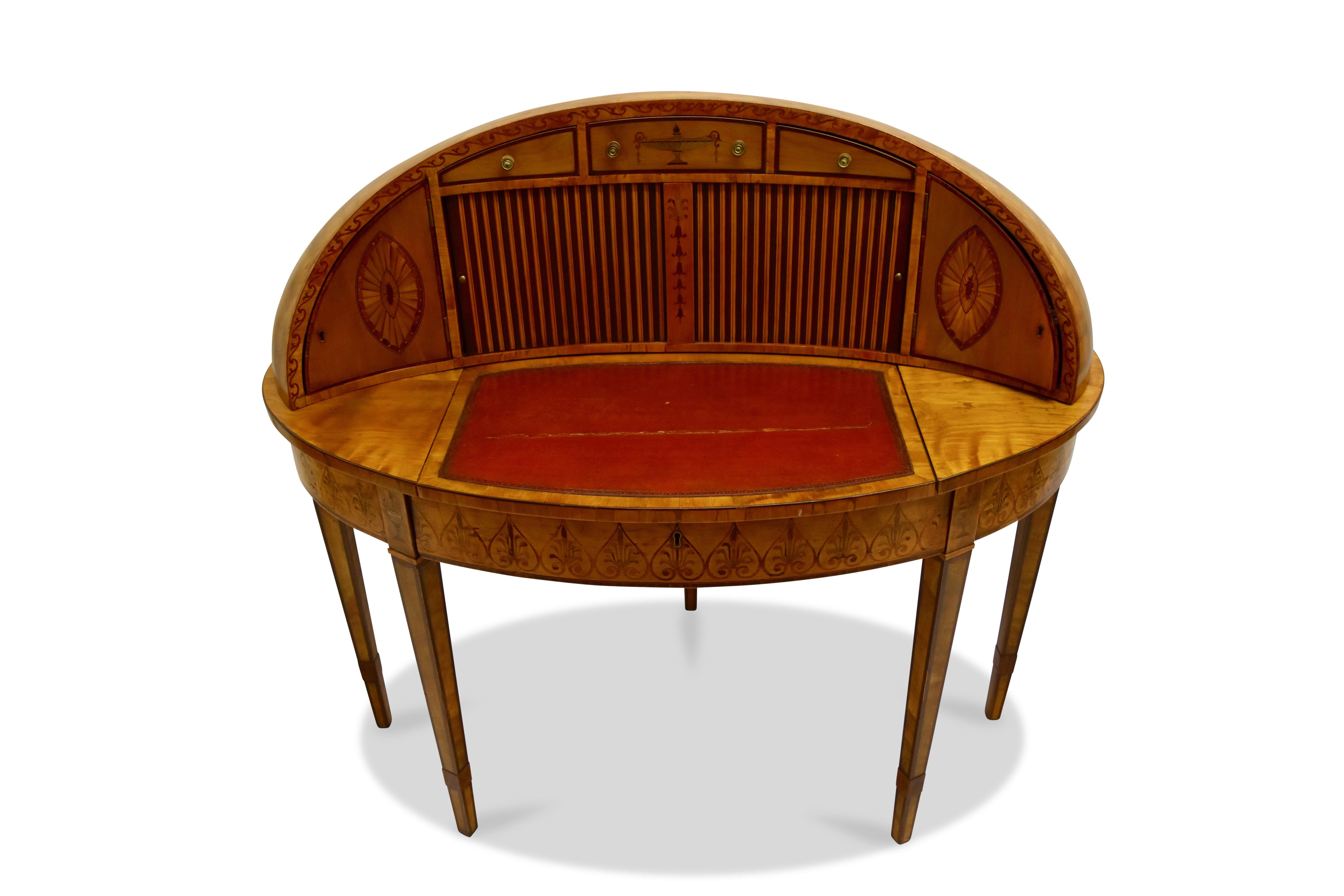 Having a satinwood veneer with fruitwood inlay, the oval shaped top with 3 drawers over a pair of tambour doors opening to reveal a fitted interior, the whole flanked by to doors and resting on an adjustable writing surface with a leather insert,
