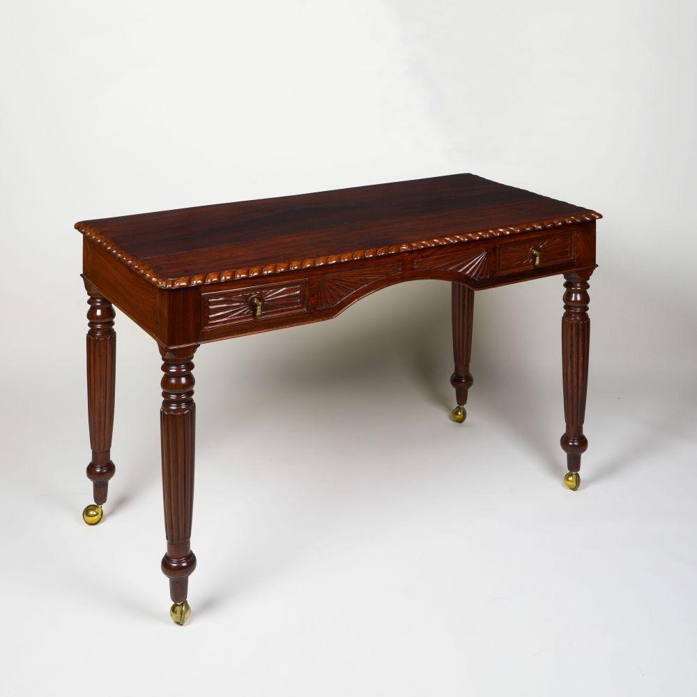 The solid rectangular top with carved gadrooned edge; over two frieze drawers with drop handles flanking an arched kneehole ,rope detail and further linear, raised on boldly turned and reeds legs on casters.