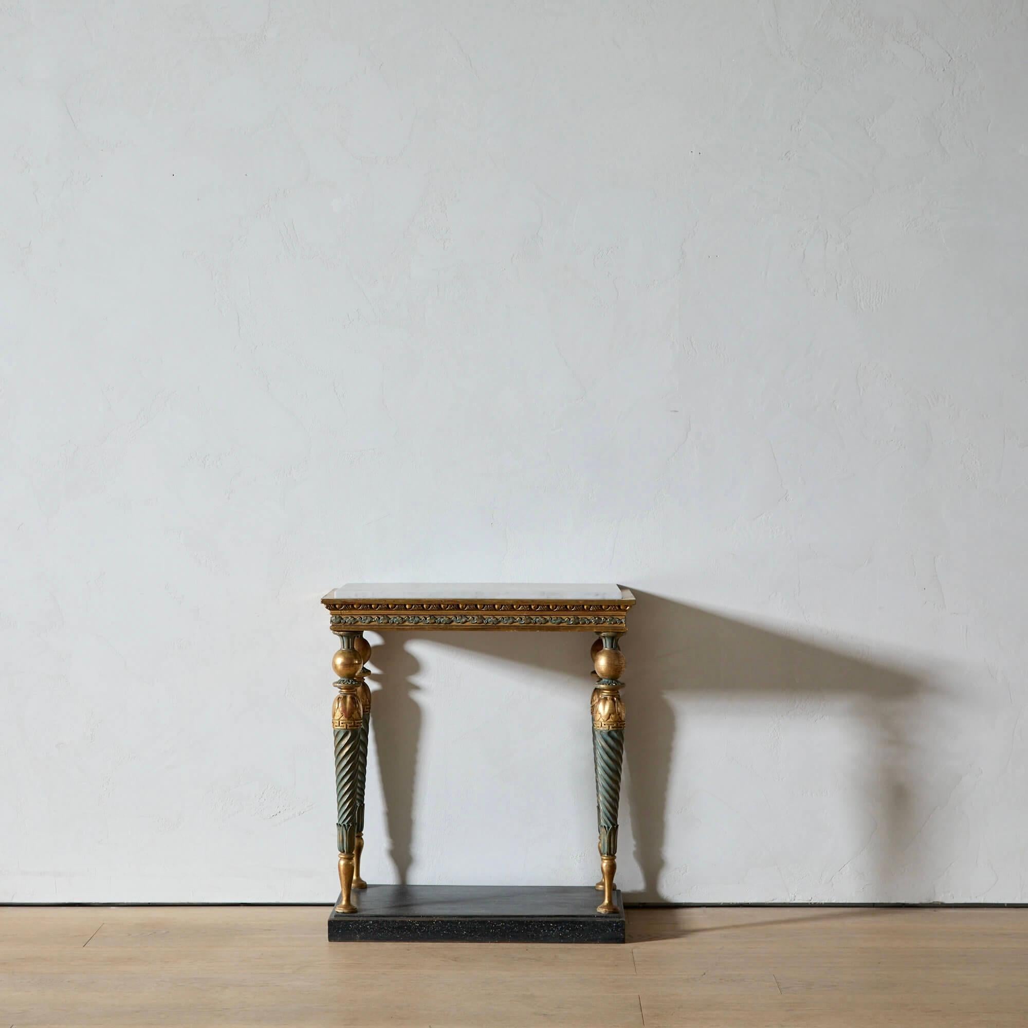 Cette table console sculptée et dorée est un bel exemple du design néoclassique suédois. Une plaque de marbre statuaire adoucie repose élégamment sur les pieds peints et dorés tournés en spirale. La base a été décorée pour ressembler à du porphyre,