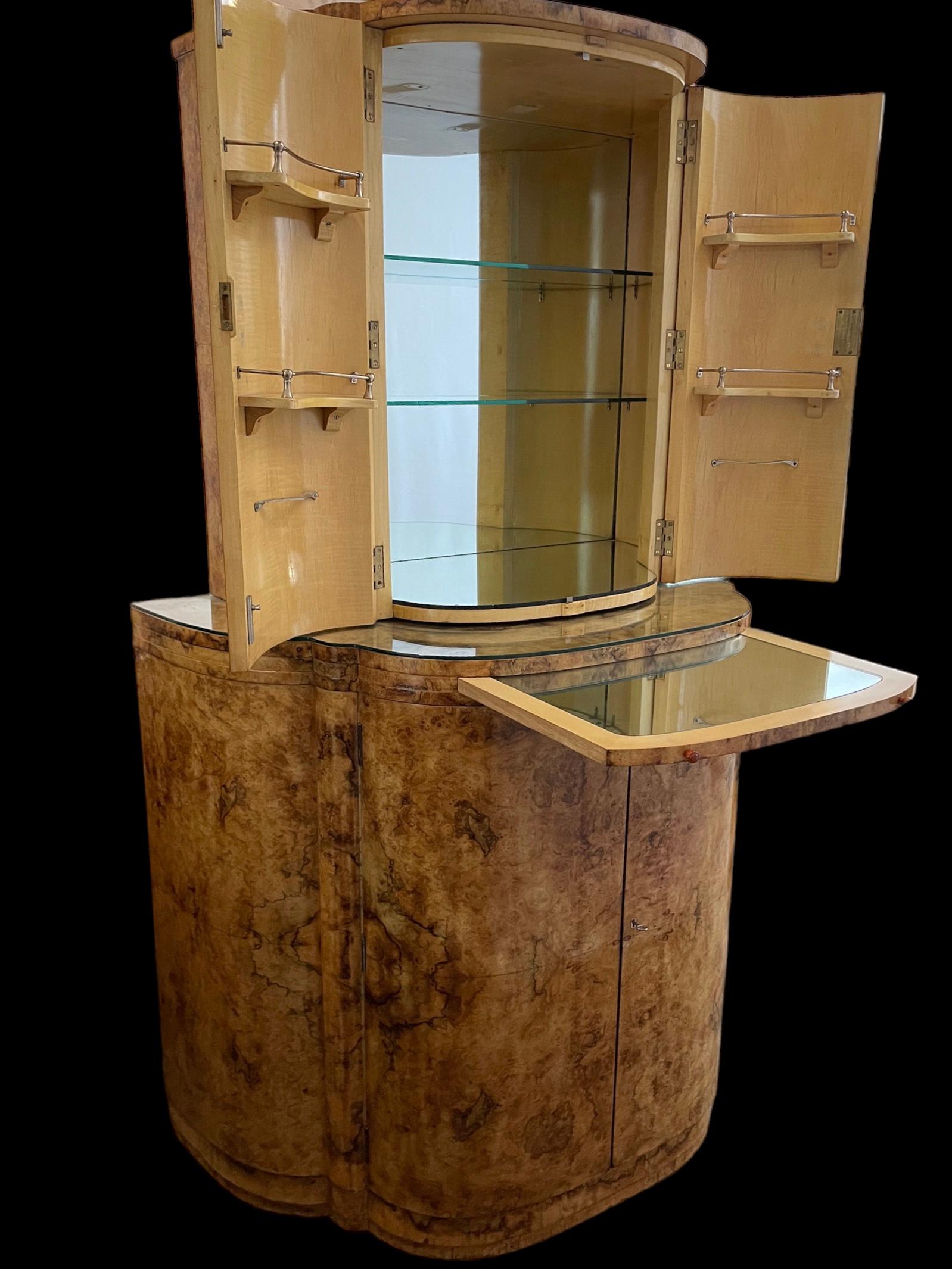 A fine Art Deco Cocktail Cabinet by Harry and Lou Epstein. In highly figured blond walnut, with the two doors to the top section, opening to reveal a maple interior with a mirrored back and base, with two glass shelves and four shelves to the two