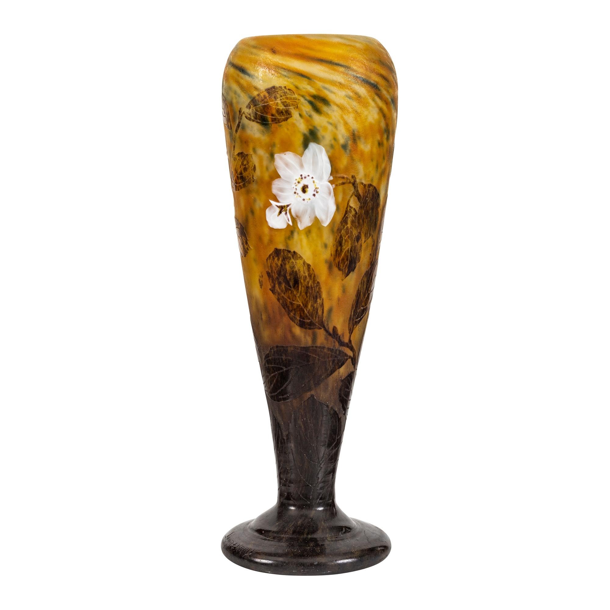 Vase en verre émaillé et camée de Daum Nancy
France, vers 1914
de forme triangulaire effilée, décorée de fleurs blanches appliquées, de feuilles vertes et de cosses fleuries sur un fond vert et jaune moucheté, reposant sur un pied