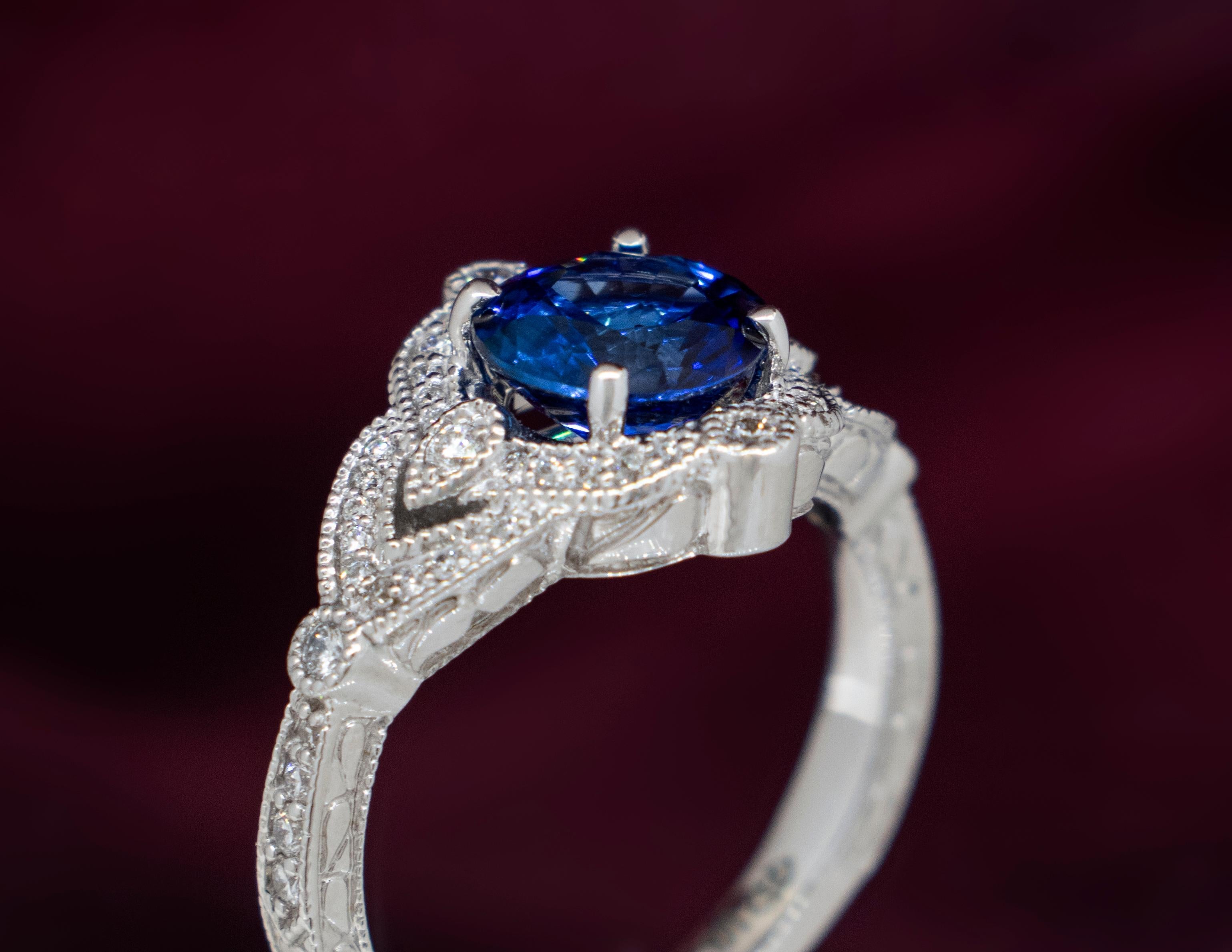 A Ladies 14K White Gold ring with sapphire center surrounded by diamonds. The Round Brilliant Sapphire is an intense cobalt blue weighing approximately 2.02 carats. It is graded as a natural, earth mined stone, Dark Tone(7), Strong Saturation (5),
