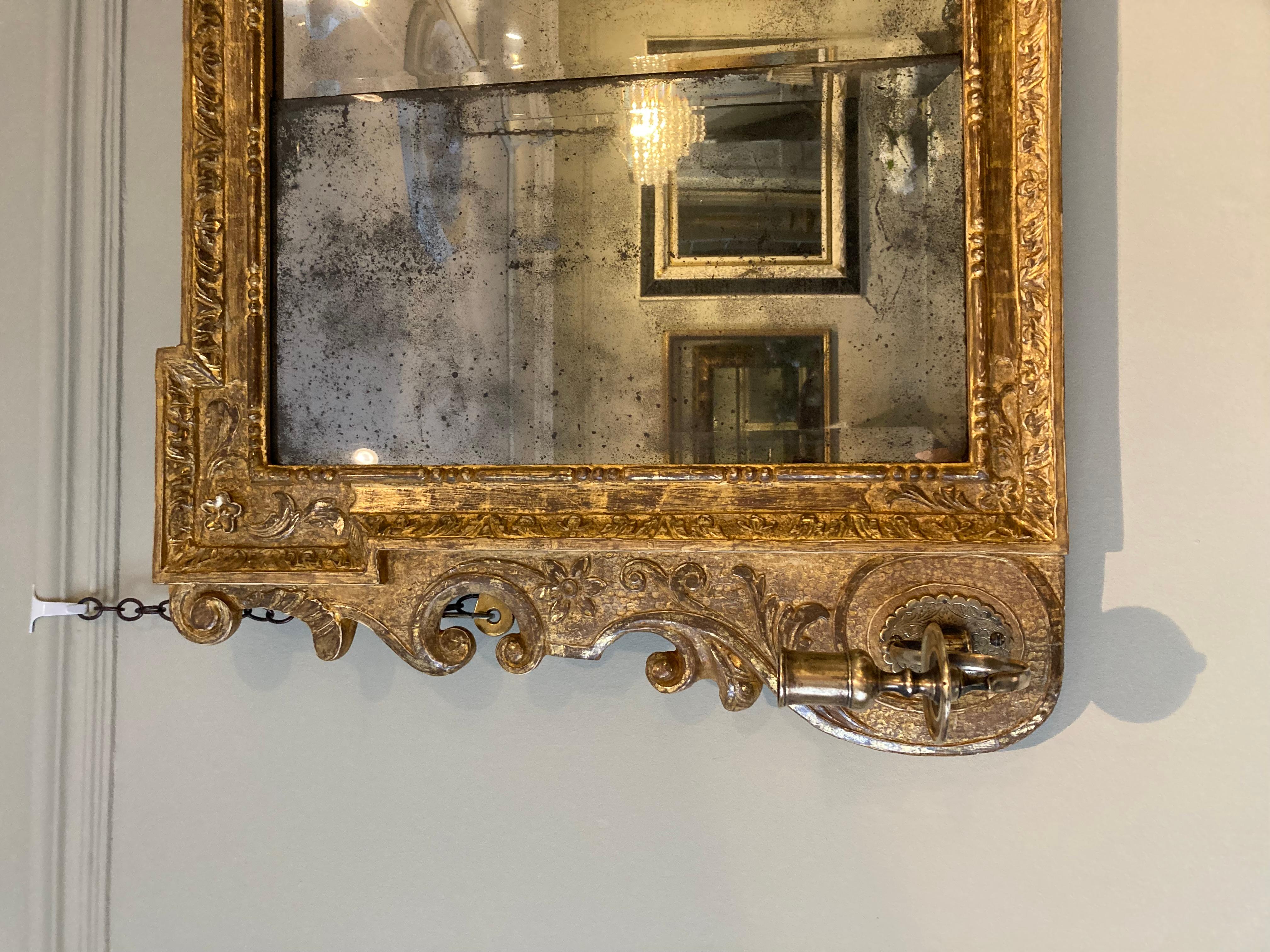 A fine early 18th Century triple-plate George II carved giltwood framed overmantle mirror of horizontal form with acanthus leaf, floral and foliate borders and scrolled sides housing two girandole candle arms. The mirror retains its original